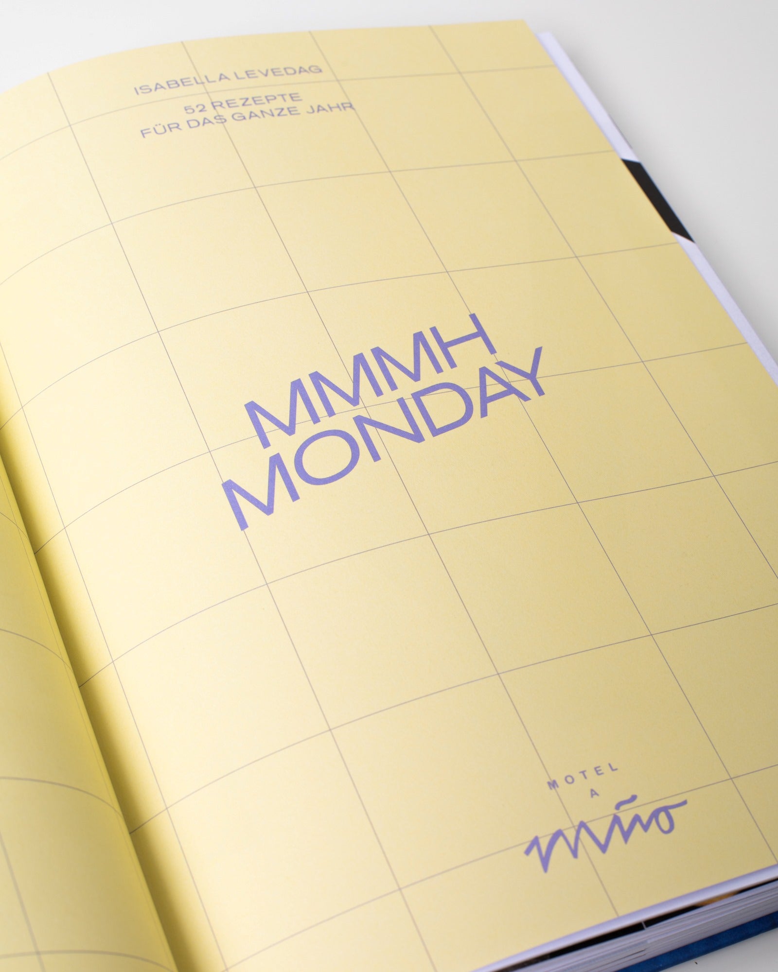 Geöffnetes Buch mit gelbem Gittermuster und lila Schrift "MMMH MONDAY", darunter "Motel a Mio".