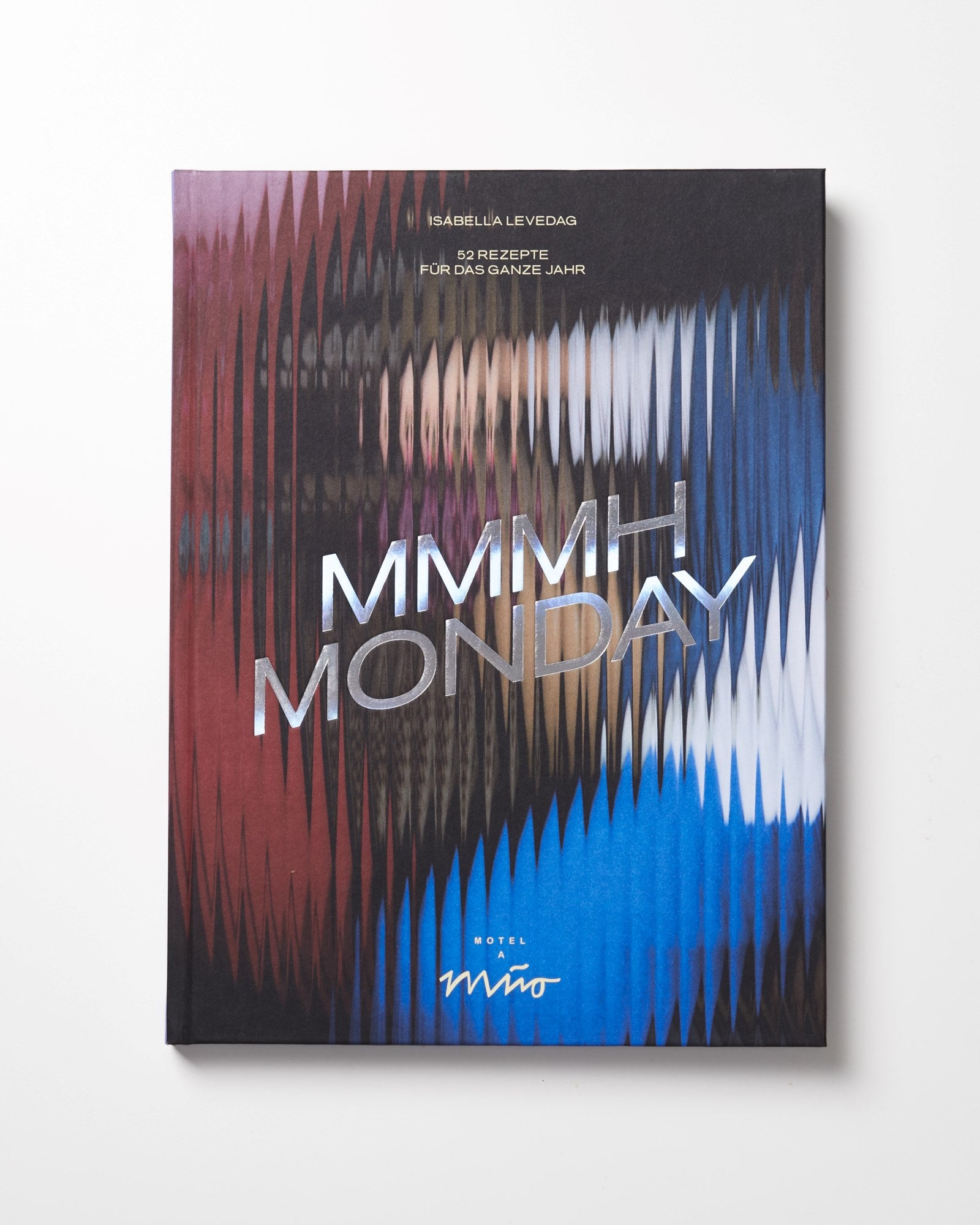 Buchcover mit einem abstrakten, wellenförmigen Muster in Rot, Blau und Weiß, der Titel "MMMHH MONDAY" in großen Buchstaben.