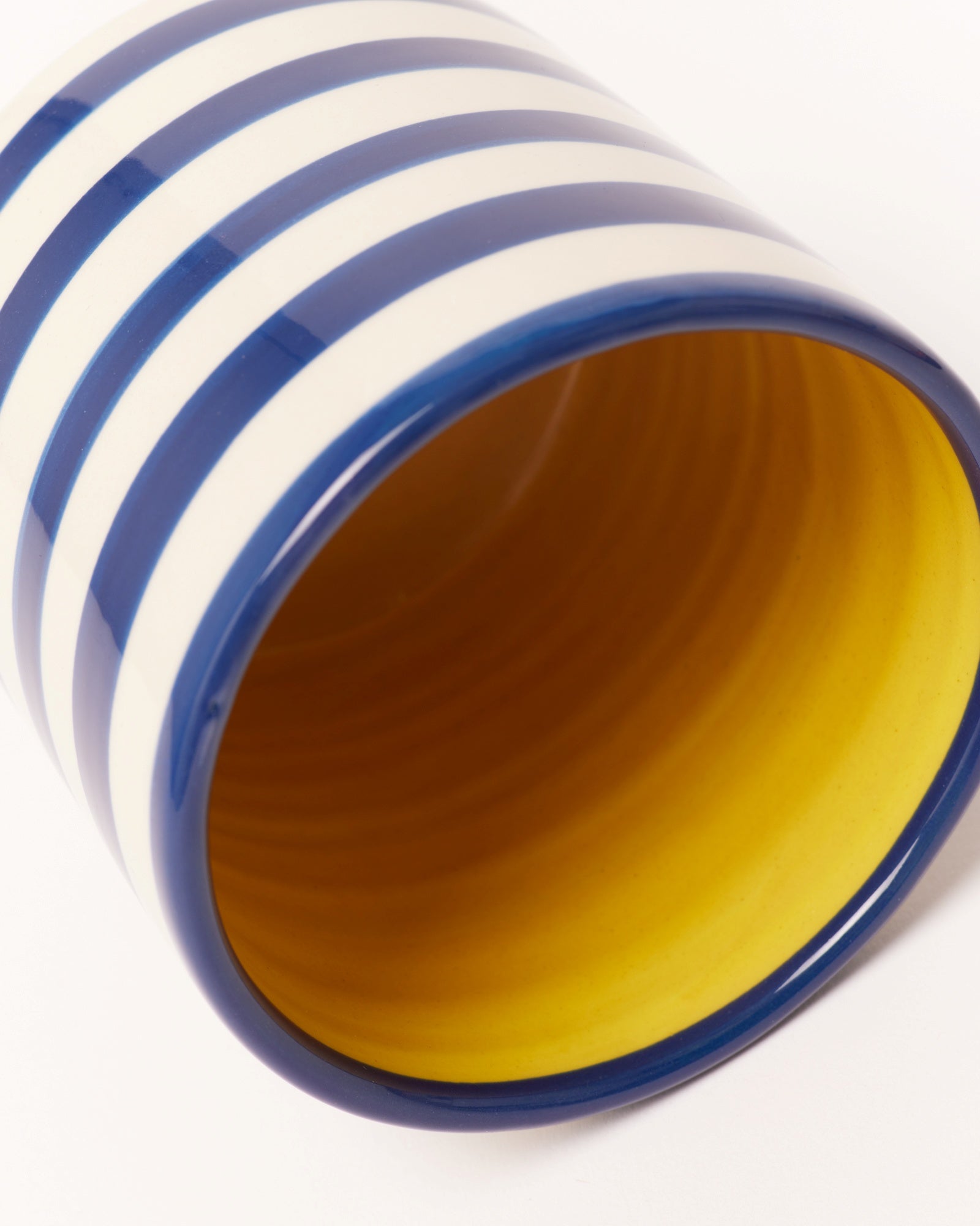 Gelbe Tasse mit blauen und weißen Streifen außen, diagonale Ansicht.