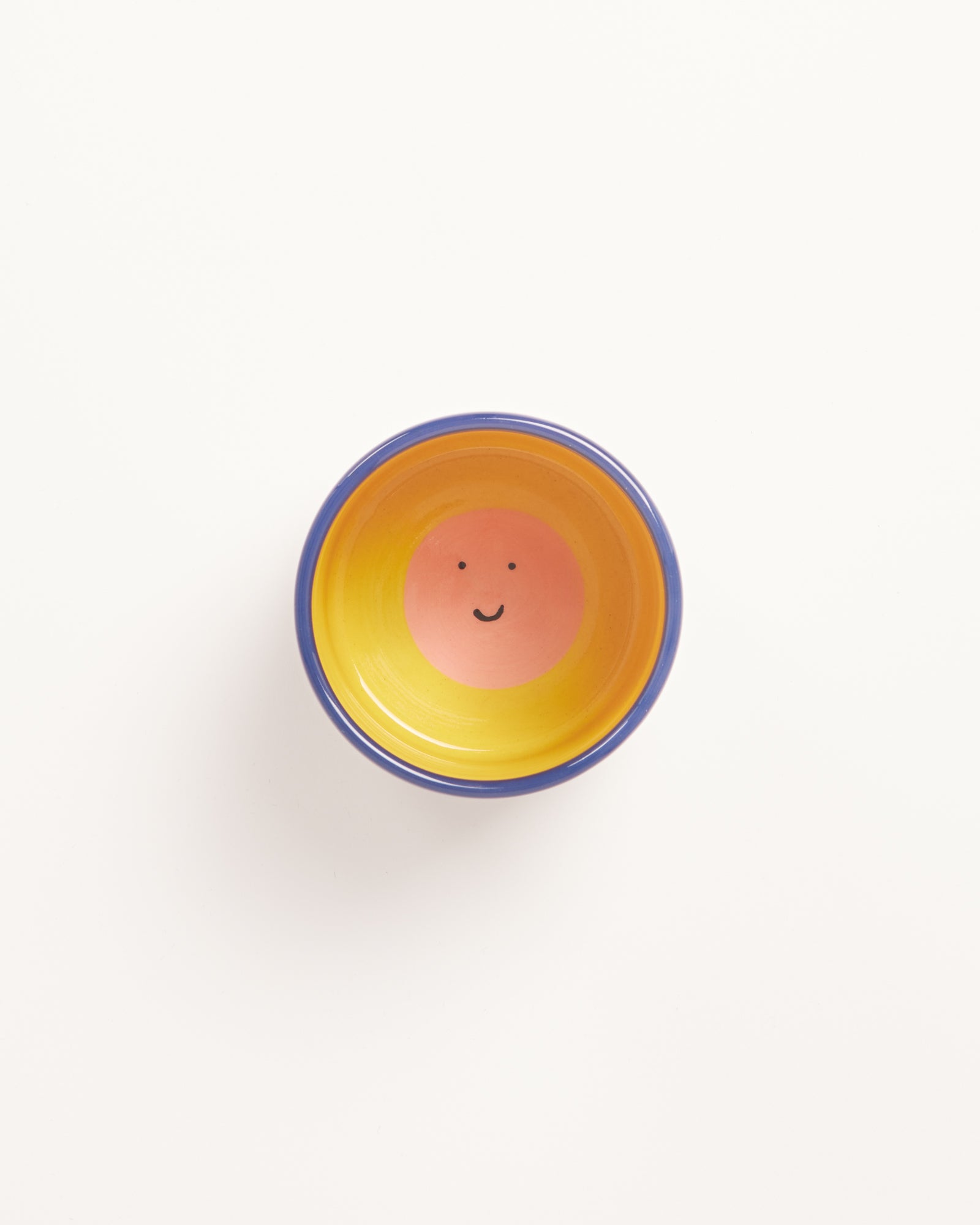 Bunte Schüssel mit gelbem Rand und fröhlichem Gesicht in der Mitte auf weißem Hintergrund.