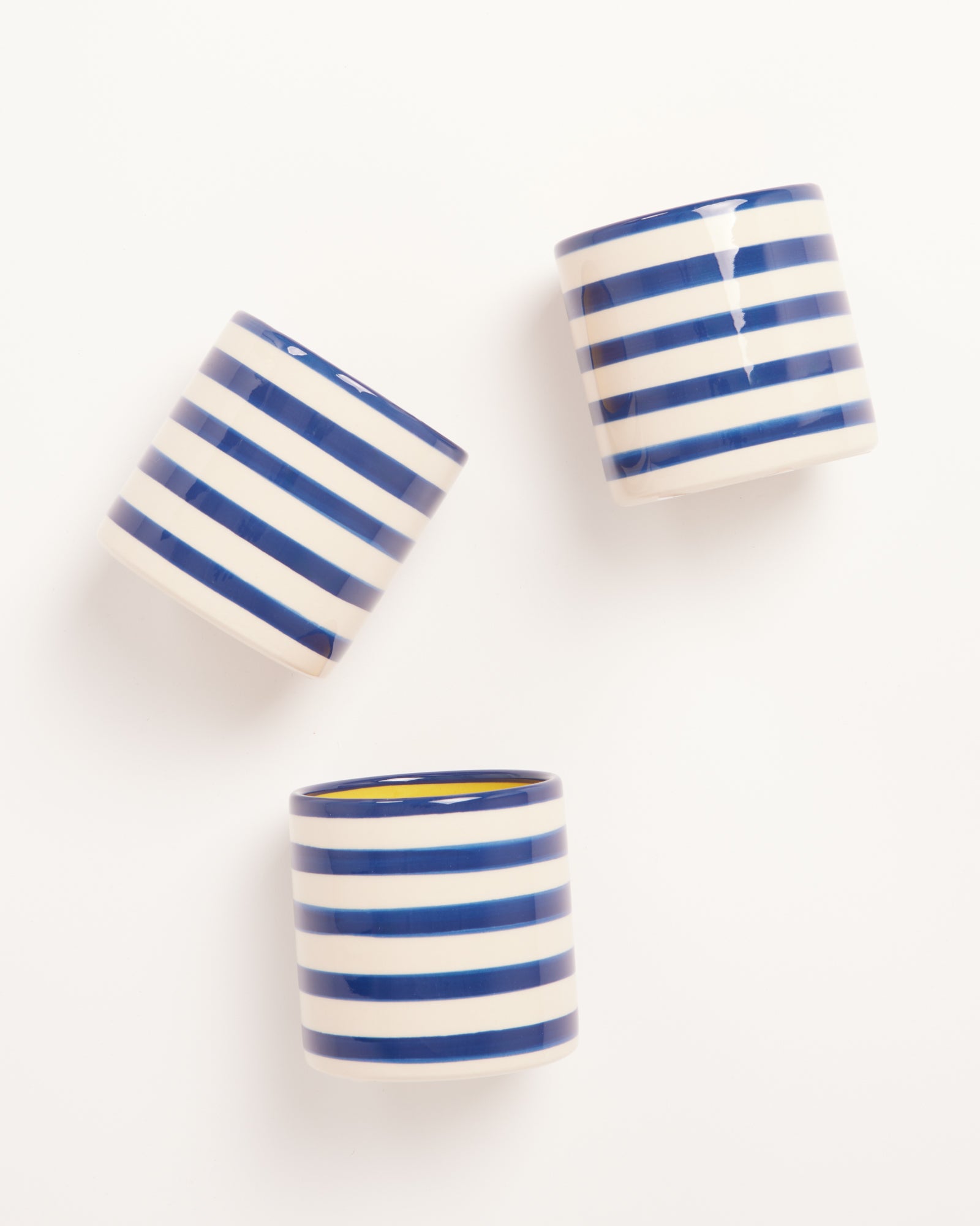 Drei blau-weiß gestreifte Becher liegen auf einem weißen Hintergrund.