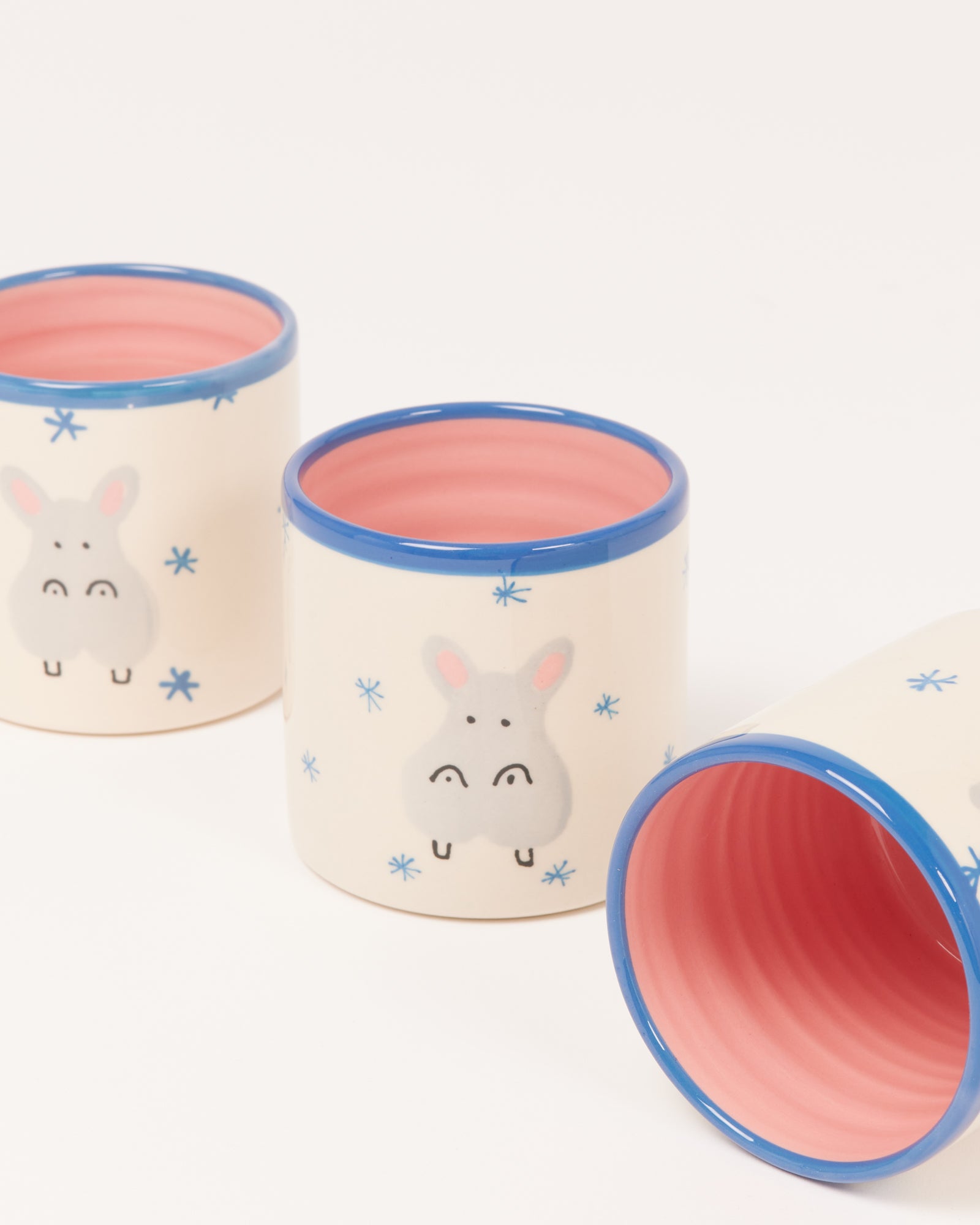 Drei cremefarbene Tassen mit blauen Rändern und Hasenmotiv, das Innere ist rosa gefärbt.