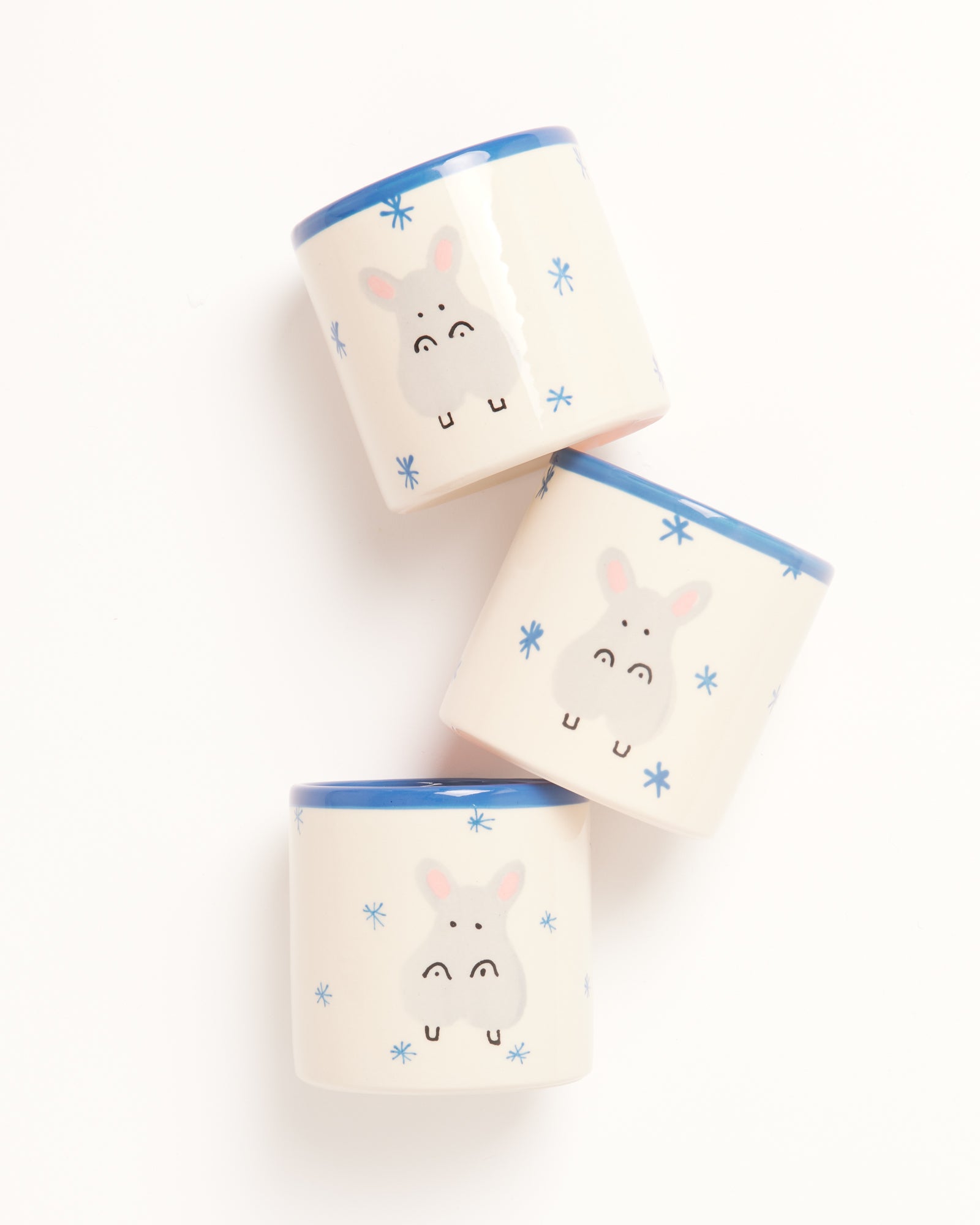 Drei weiße Becher mit blauen Rändern und niedlichen Tiermotiven, schräg auf weißem Hintergrund platziert.