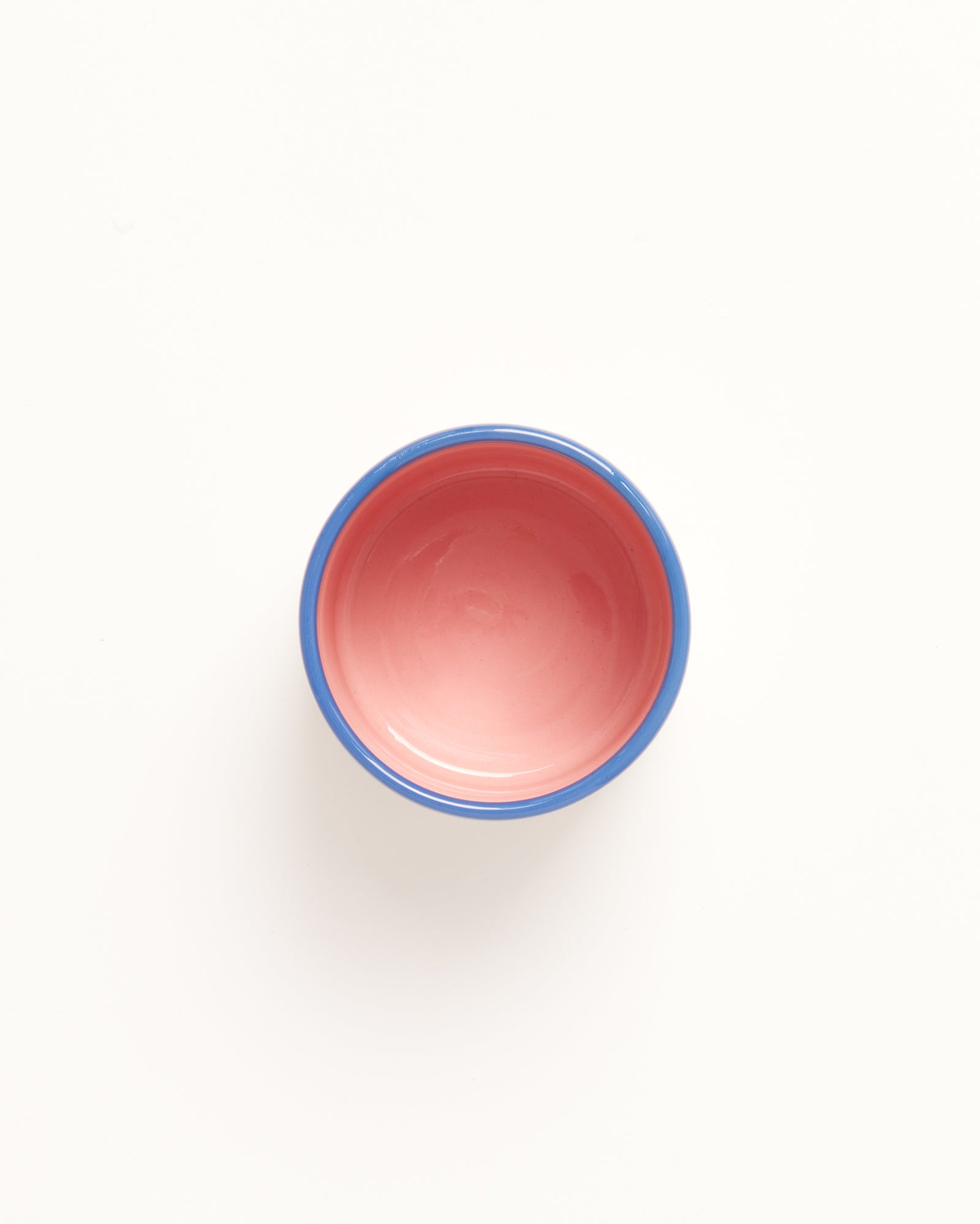 Kleine Schale mit rosa Innenseite und blauem Rand auf weißem Hintergrund, von oben betrachtet.