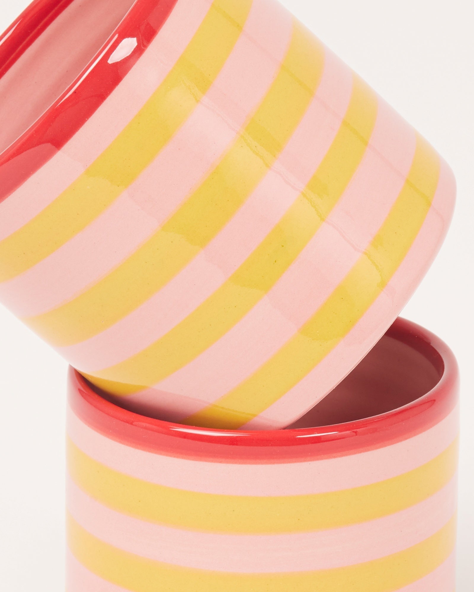 Zwei gestreifte Keramikbecher in Pink und Gelb mit rotem Rand, die ineinander gestapelt sind.