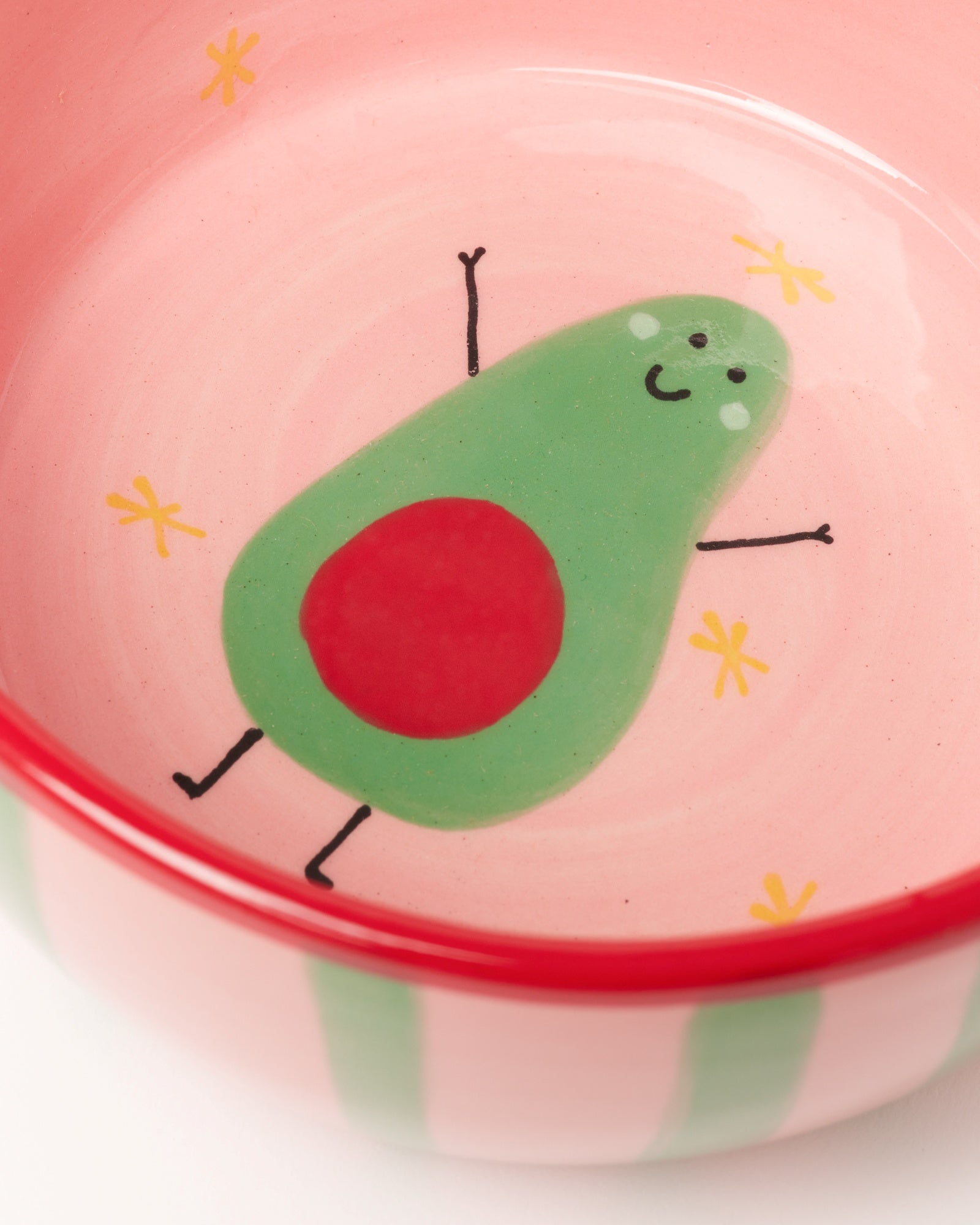Schale mit rotem Rand und einem fröhlichen, tanzenden Avocado-Design auf rosa Hintergrund mit gelben Sternchen.