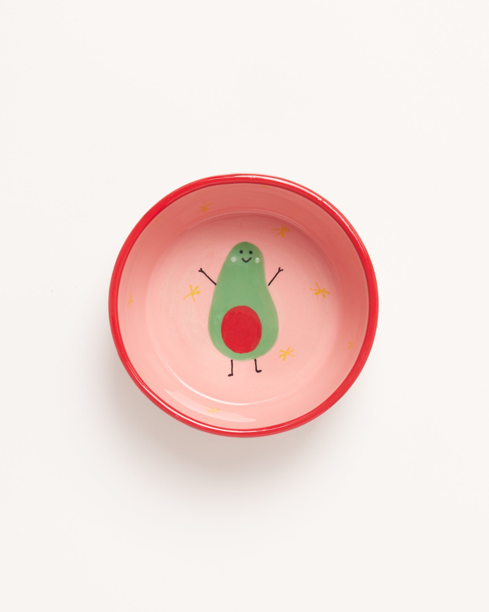 Bunte Schüssel mit lustigem Avocado-Motiv in der Mitte, umgeben von gelben Sternen auf rosa Hintergrund.