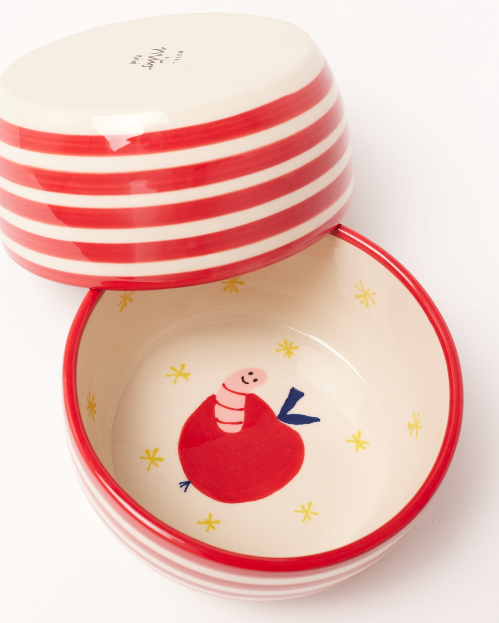 Zwei Keramikschalen mit roten Streifen, eine zeigt einen Cartoon-Wurm in einem Apfel auf dem Boden der Schale.