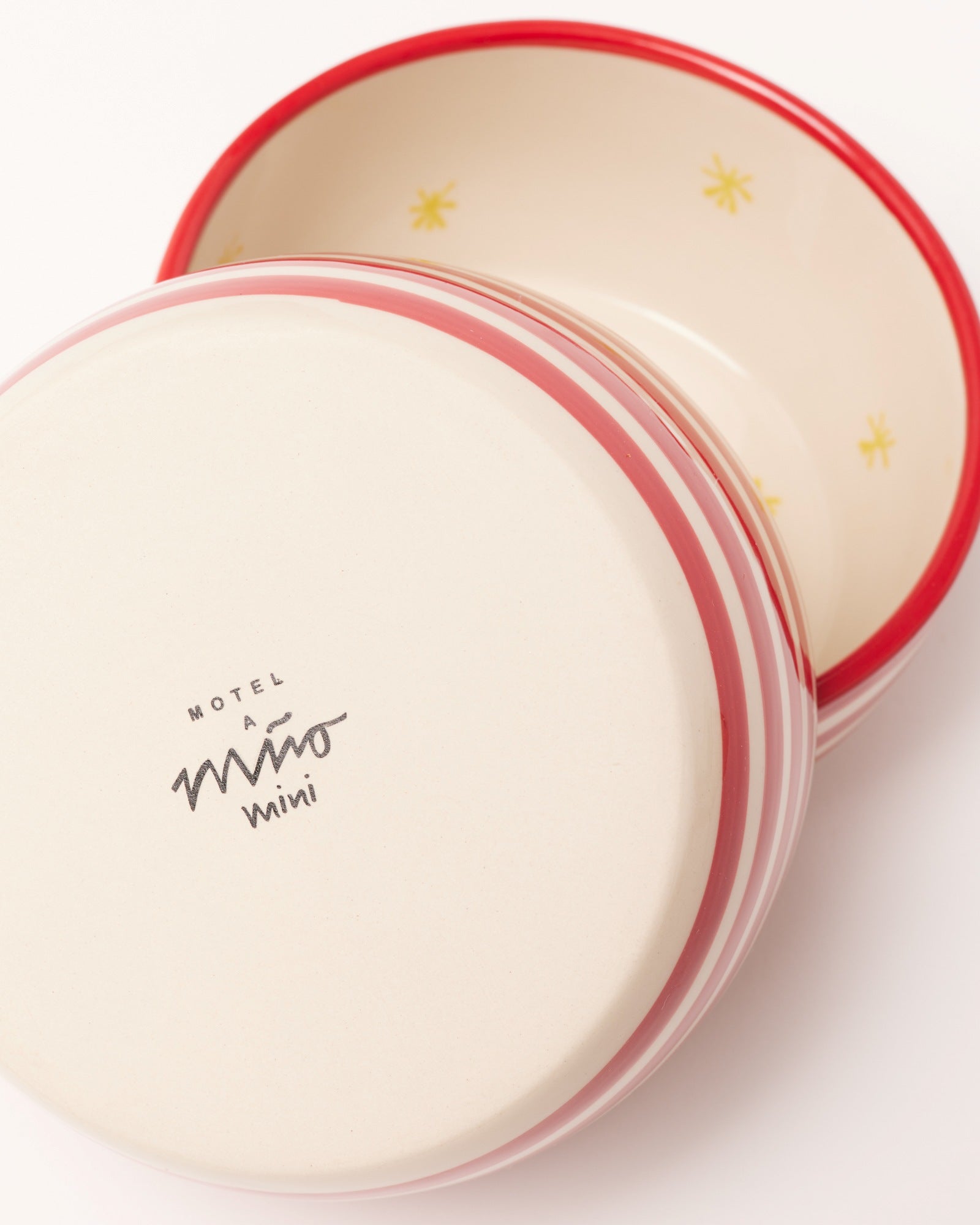 Zwei ineinandergestapelte, cremefarbene Keramikschalen mit roten Streifen und gelben Sternen, eine hat den Schriftzug "Motel a Mió mini".