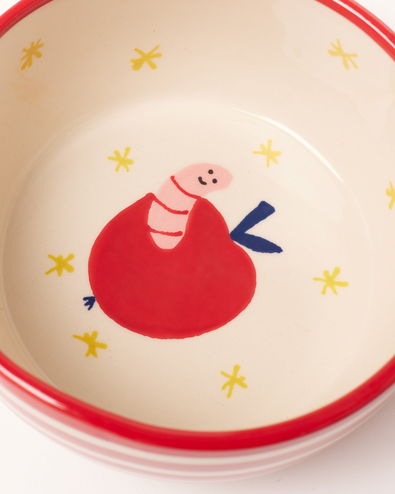 Keramikschüssel mit gemaltem roten Apfel und Wurm, umgeben von gelben Sternen, auf weißem Hintergrund.