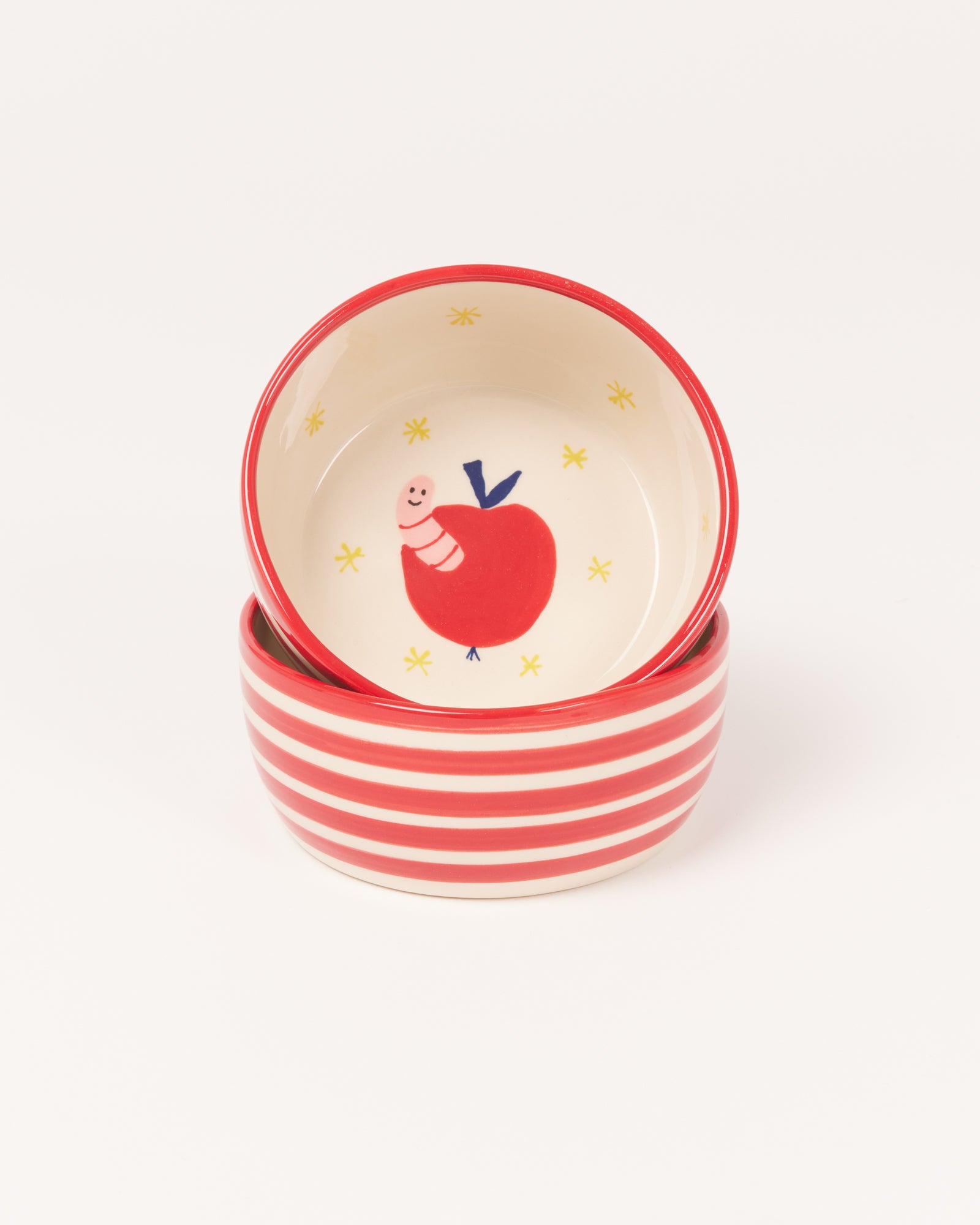 Zwei gestapelte Schüsseln mit roten und weißen Streifen, eine mit einem Apfel- und Wurm-Muster im Inneren.