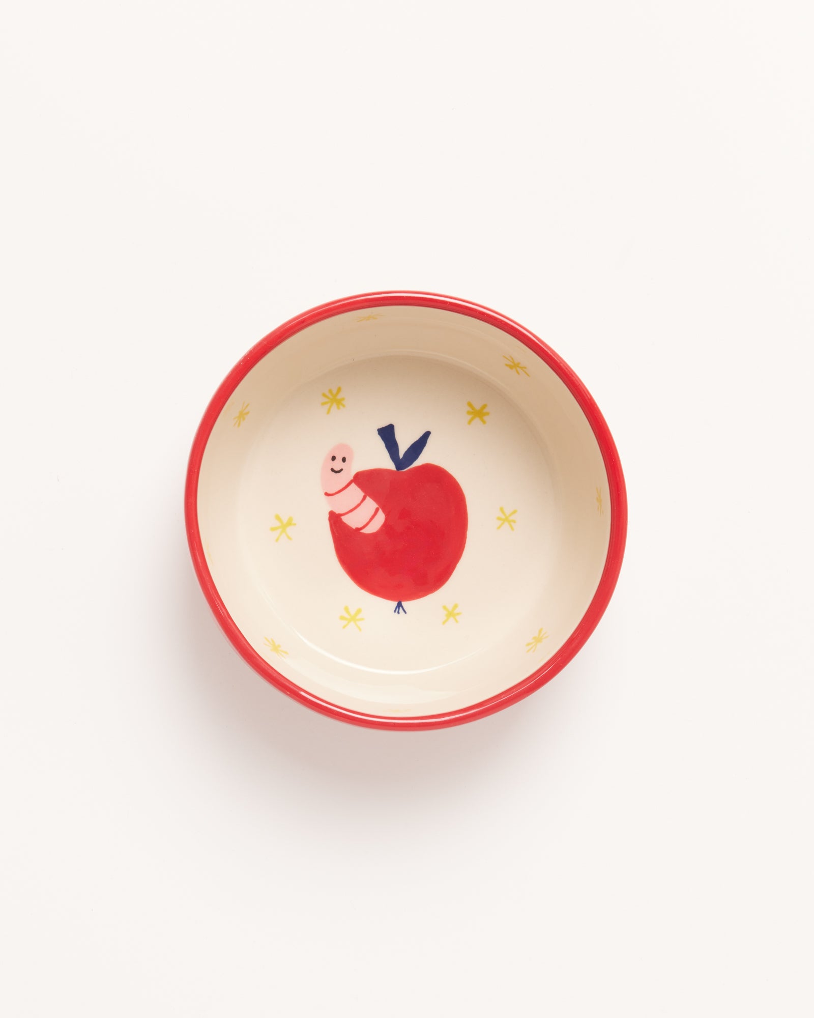 Kleine Schale mit rotem Rand, innen ein Bild von einem Apfel und einer Raupe auf hellem Hintergrund mit gelben Sternen.