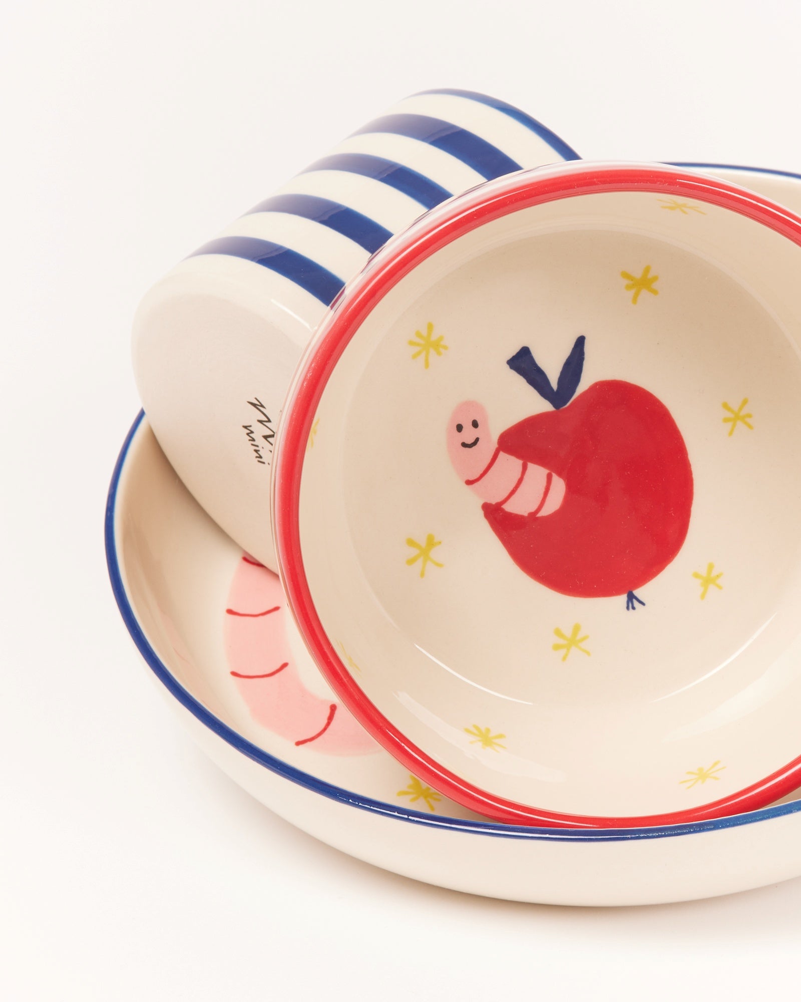 Zwei bunte Keramikteller, einer mit einem Apfelmotiv und der andere mit blauen Streifen, übereinander gestapelt.