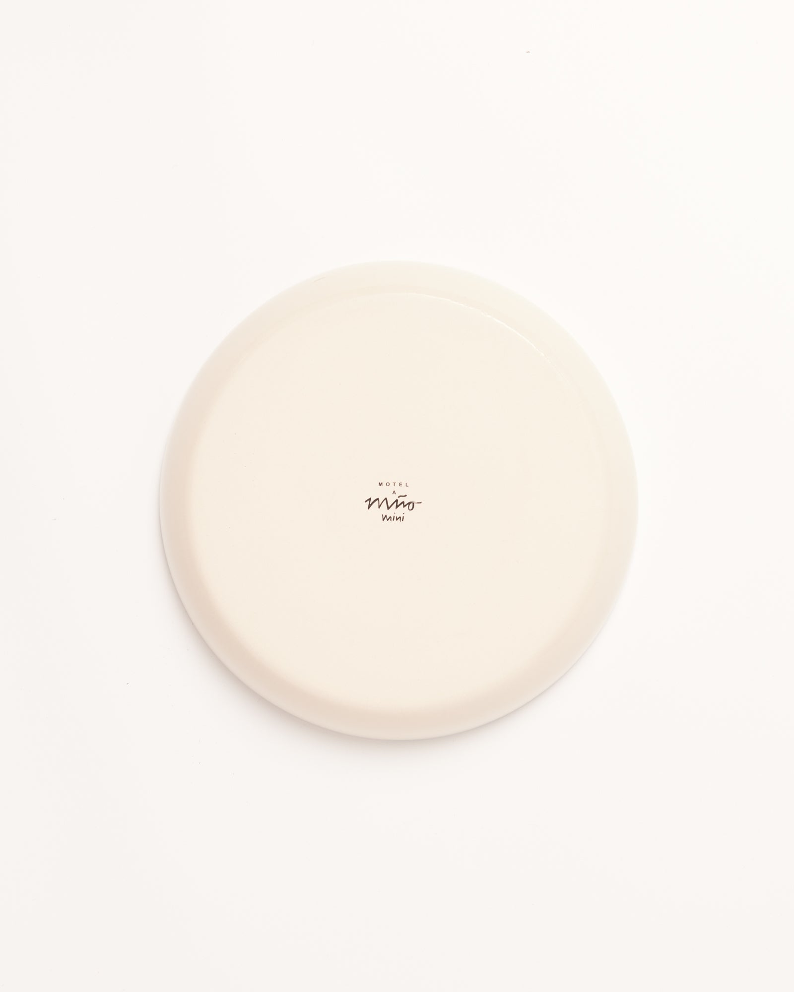 Ein beiger Teller mit der Aufschrift "Motel Miro Mini" auf einer weißen Oberfläche.