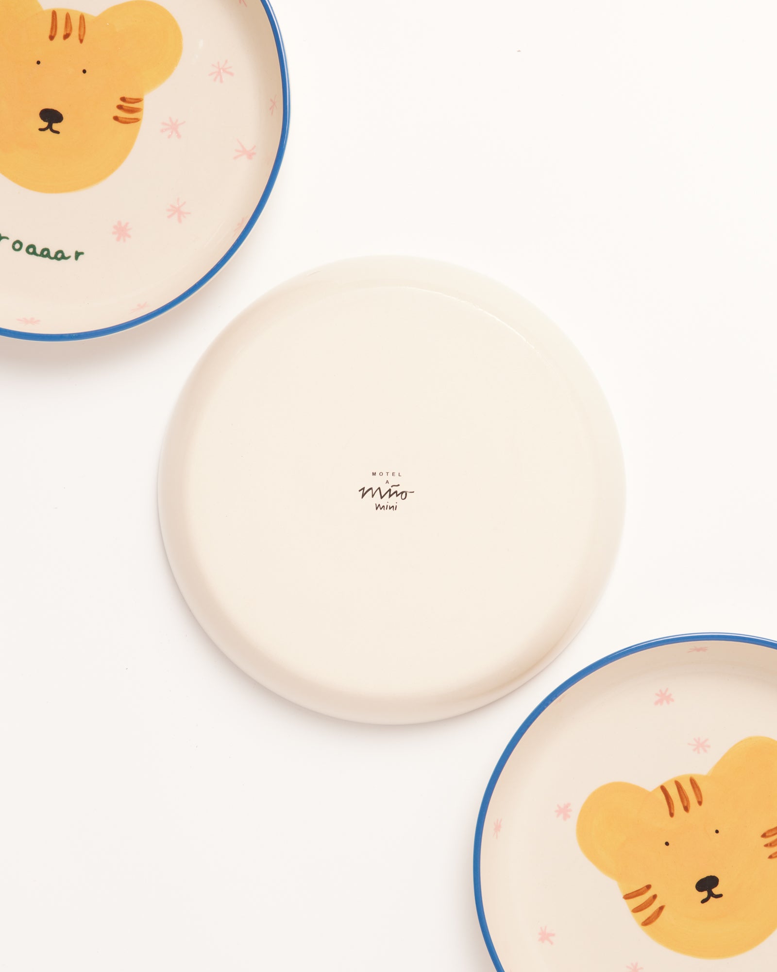 Drei Teller, zwei mit Tiergesicht und blauer Kante, einer schlicht mit "Motel a Mio Wini" Schriftzug.