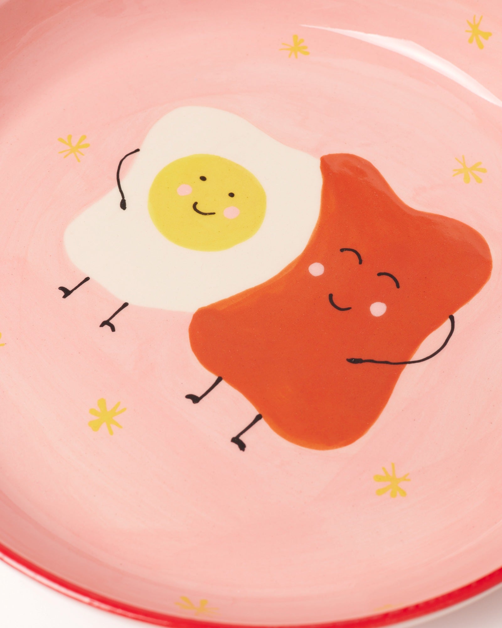 Niedliche Zeichnung eines lächelnden Spiegeleis und Toasts auf einem rosa Teller mit kleinen gelben Sternen.