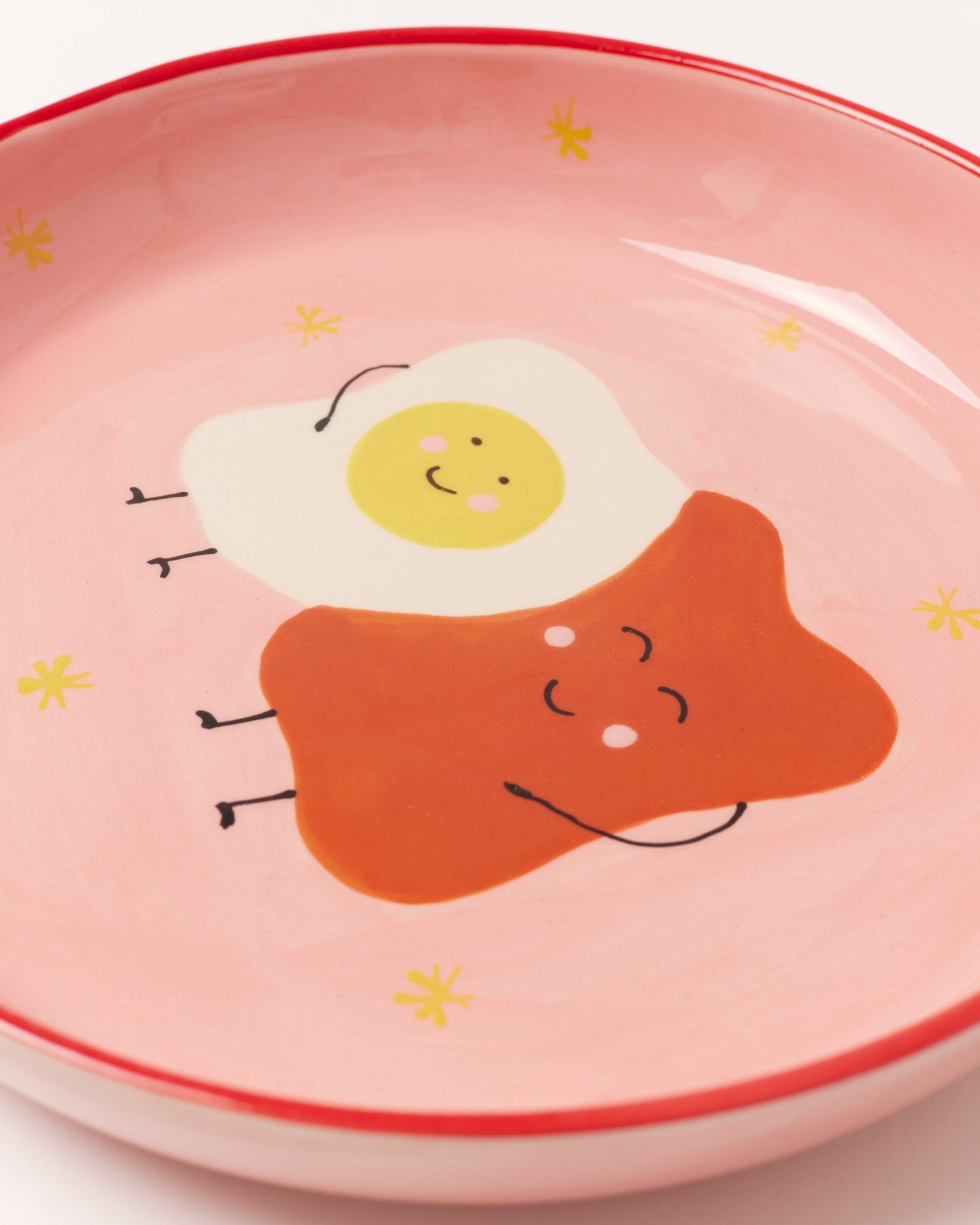 Rosa Teller mit lustigem Spiegelei und Brot Gesichtern, umgeben von kleinen gelben Sternen.