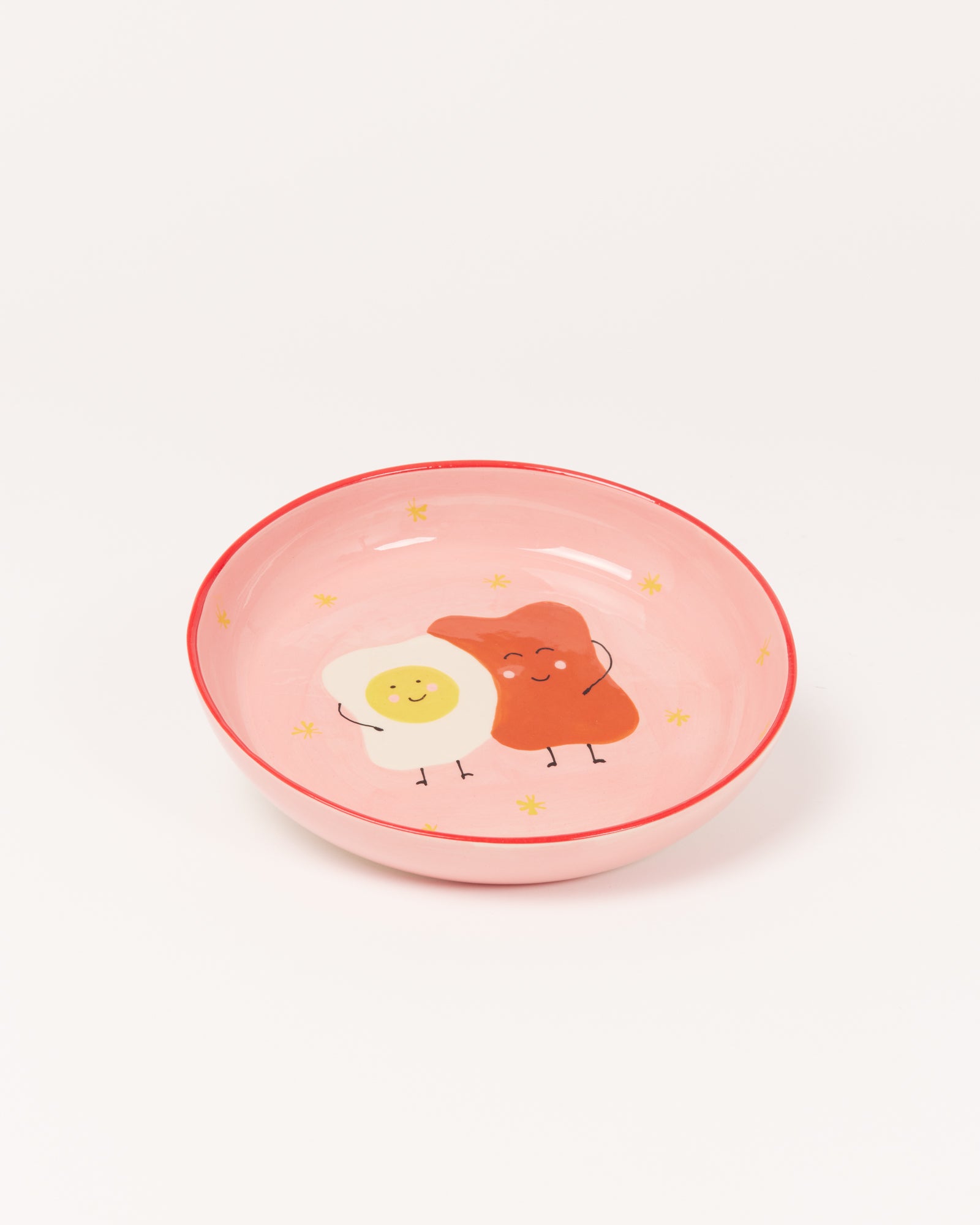 Rosa Schüssel mit fröhlichen Zeichnungen eines Eis und eines Specks auf dem Boden, umgeben von kleinen gelben Sternen.