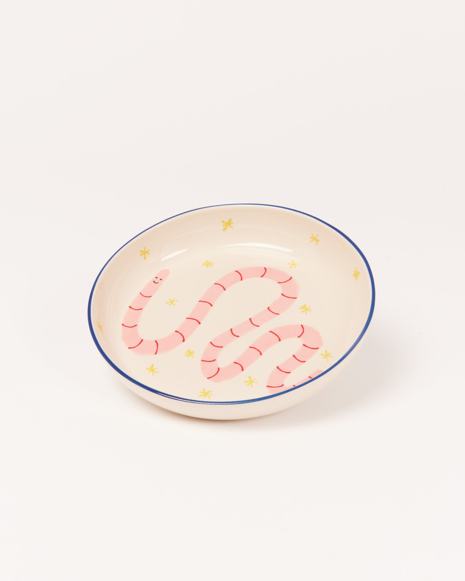 Keramikschale mit einem gemalten rosa Wurm und gelben Sternen auf hellem Hintergrund.
