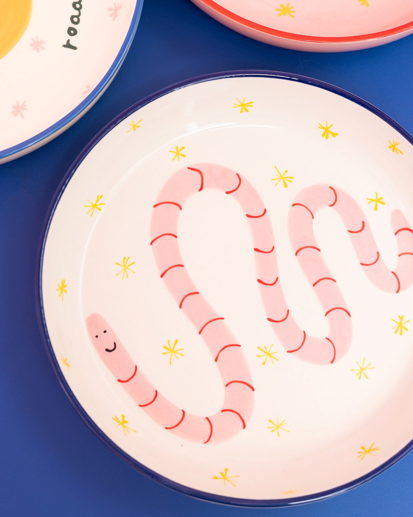 Bunter Teller mit einem lachenden Regenwurm-Muster auf blauem Hintergrund.