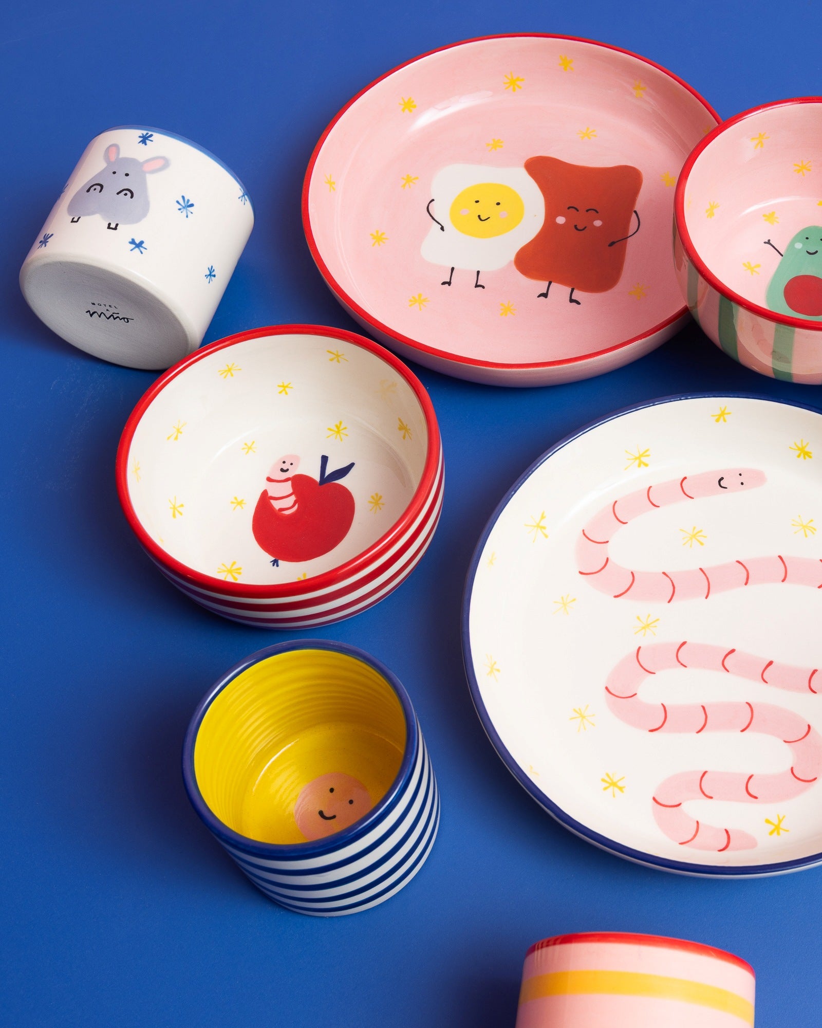 Bunte Keramikschalen und Tassen auf blauem Hintergrund mit niedlichen Motiven wie Eiern und Würmern.