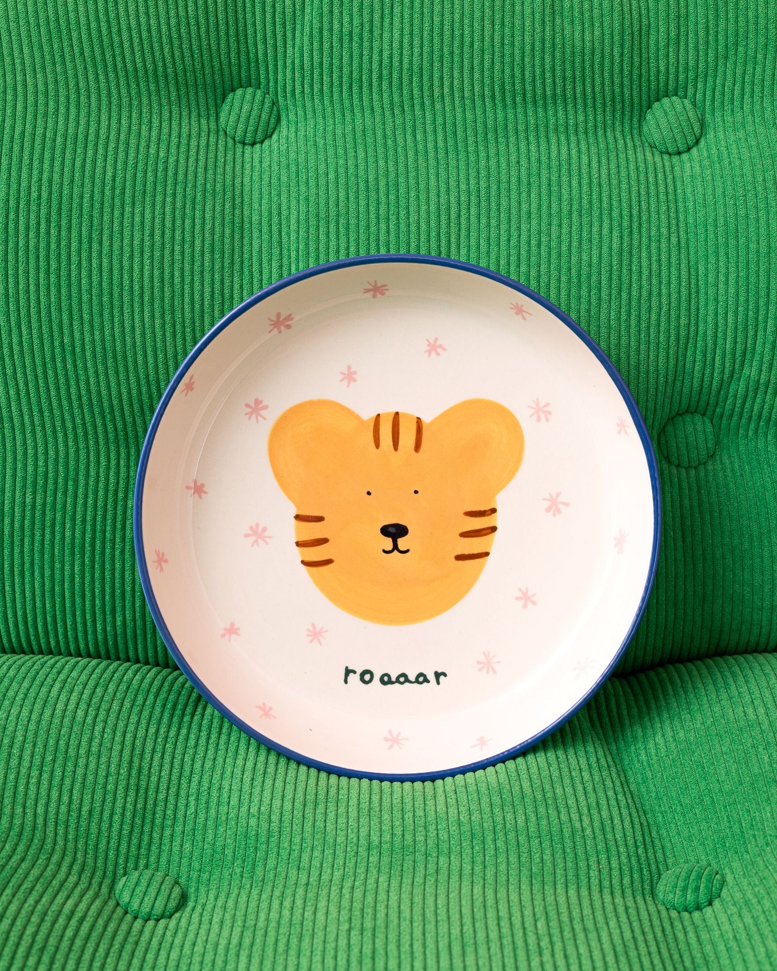 Ein Teller mit einem gemalten Tiger und dem Wort "roaaar" liegt auf einem grünen, gerippten Kissen.