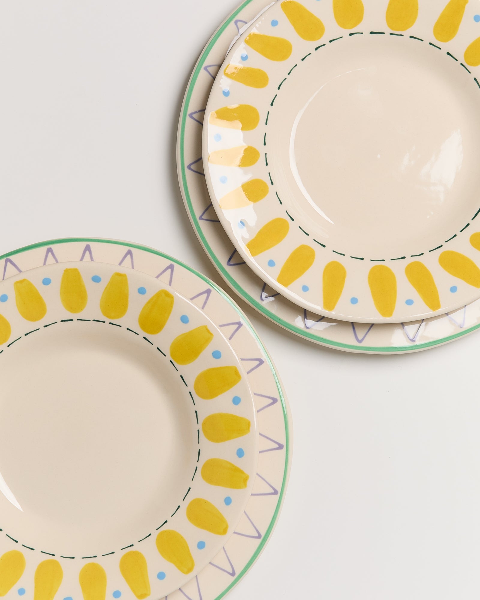 Zwei Teller mit gelbem und blauem Punktmuster sowie grüner Bordüre auf beigem Hintergrund.