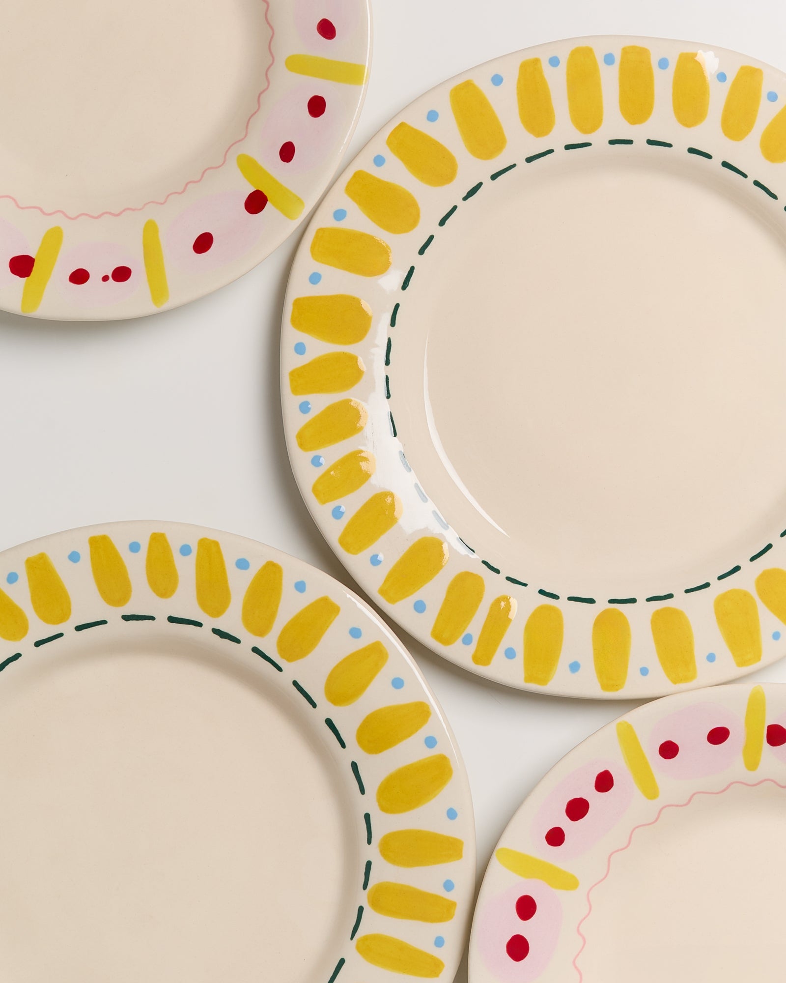 Vier Teller mit bunten Randmustern in Gelb, Rosa und Rot auf weißem Hintergrund.