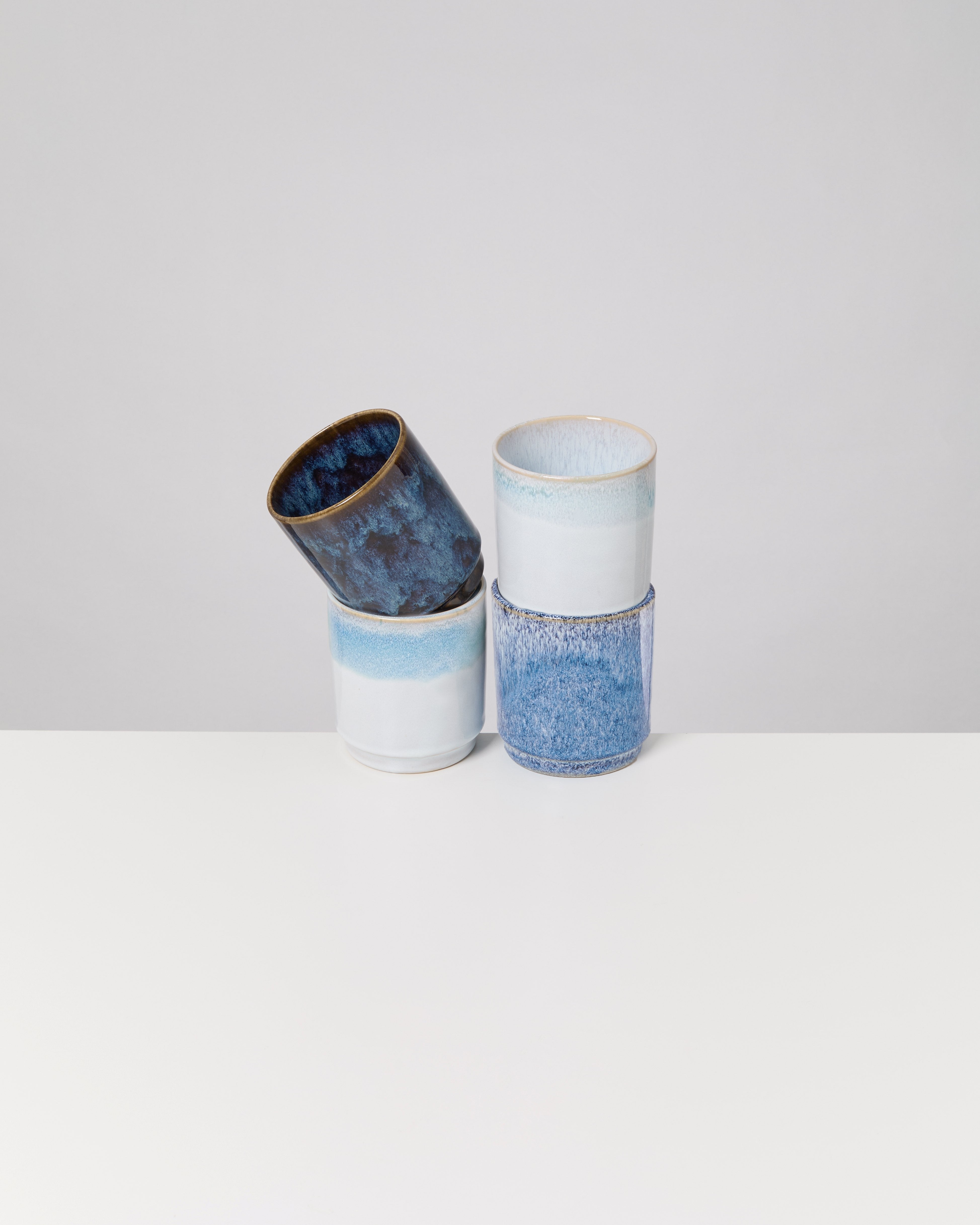 Drei blaue Keramikbecher übereinander gestapelt, auf einem weißen Hintergrund.