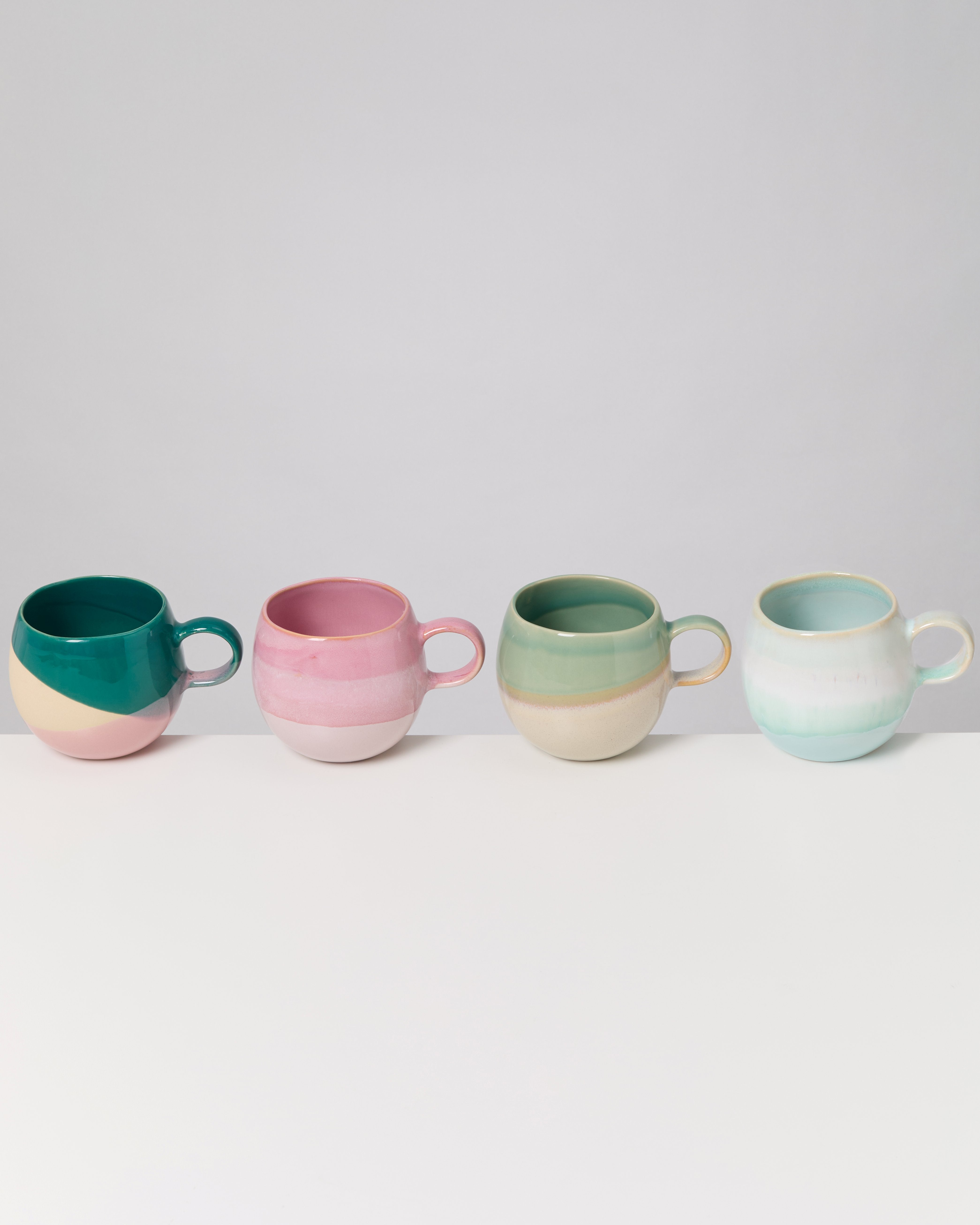 Vier bunte Kaffeetassen in einer Reihe auf einem weißen Tisch vor grauem Hintergrund.