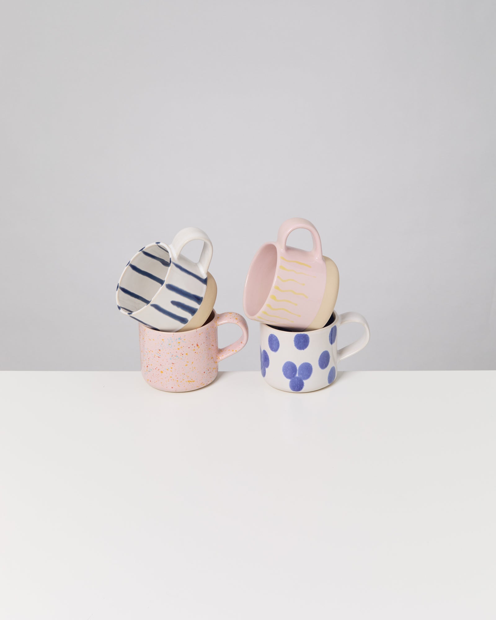 Vier bunte Tassen mit verschiedenen Mustern sind auf einem weißen Tisch gestapelt.