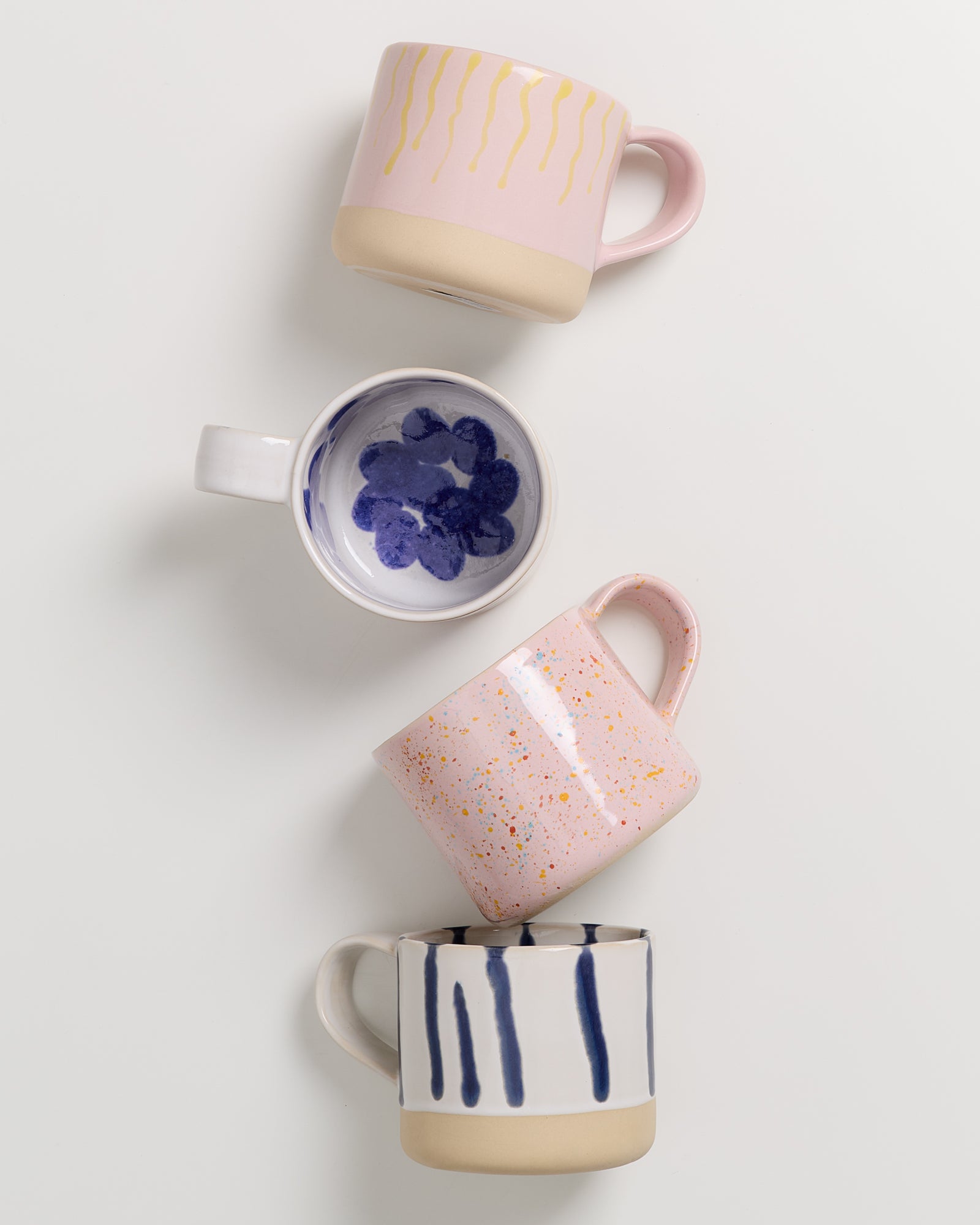 Vier bunte Tassen liegen übereinander auf einem weißen Hintergrund.