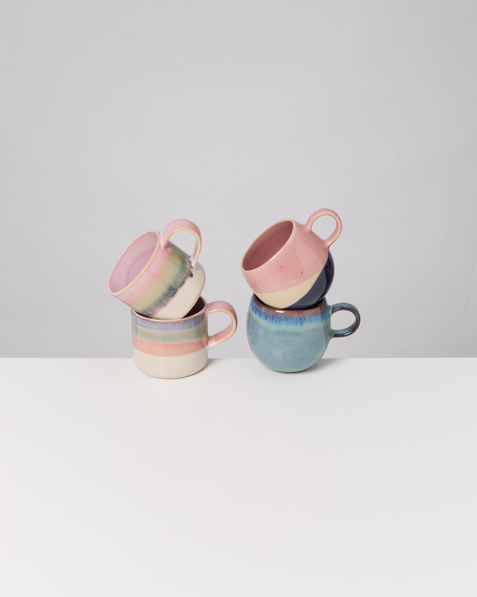 Vier bunte Keramiktassen auf einem weißen Tisch, zwei gestapelt links, zwei gestapelt rechts.