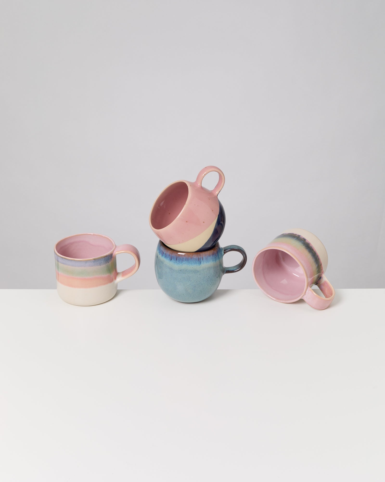 Drei pastellfarbene Keramiktassen, zwei gestapelt, auf einem weißen Tisch.