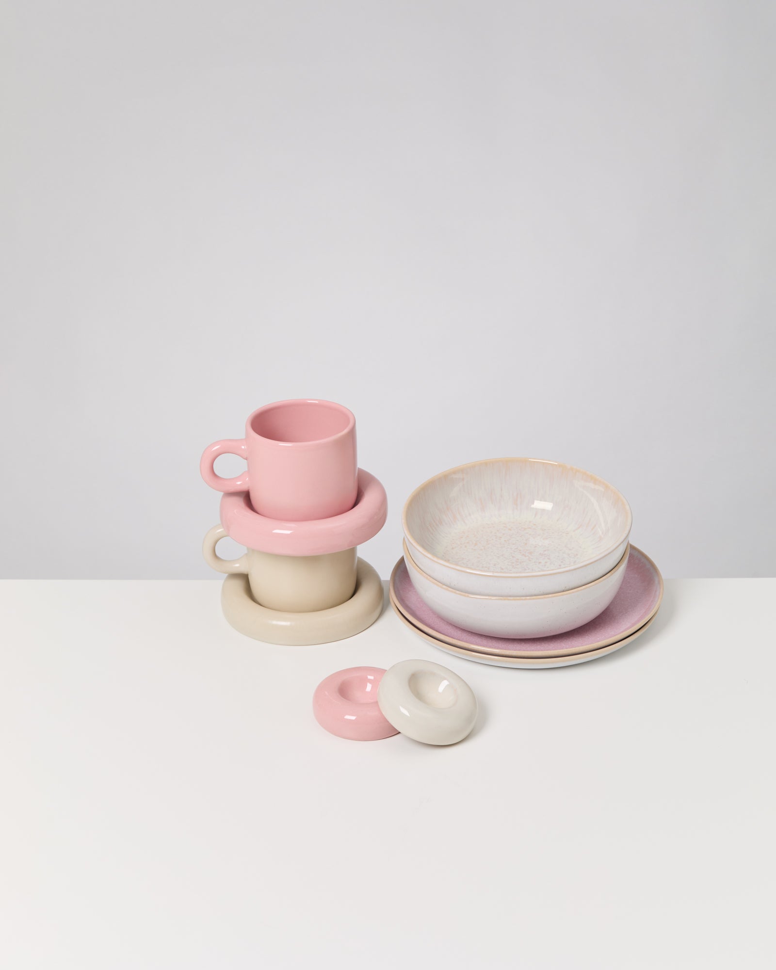 Gestapelte rosa und beigen Tassen, dazu passende Schalen und Teller auf weißem Hintergrund.