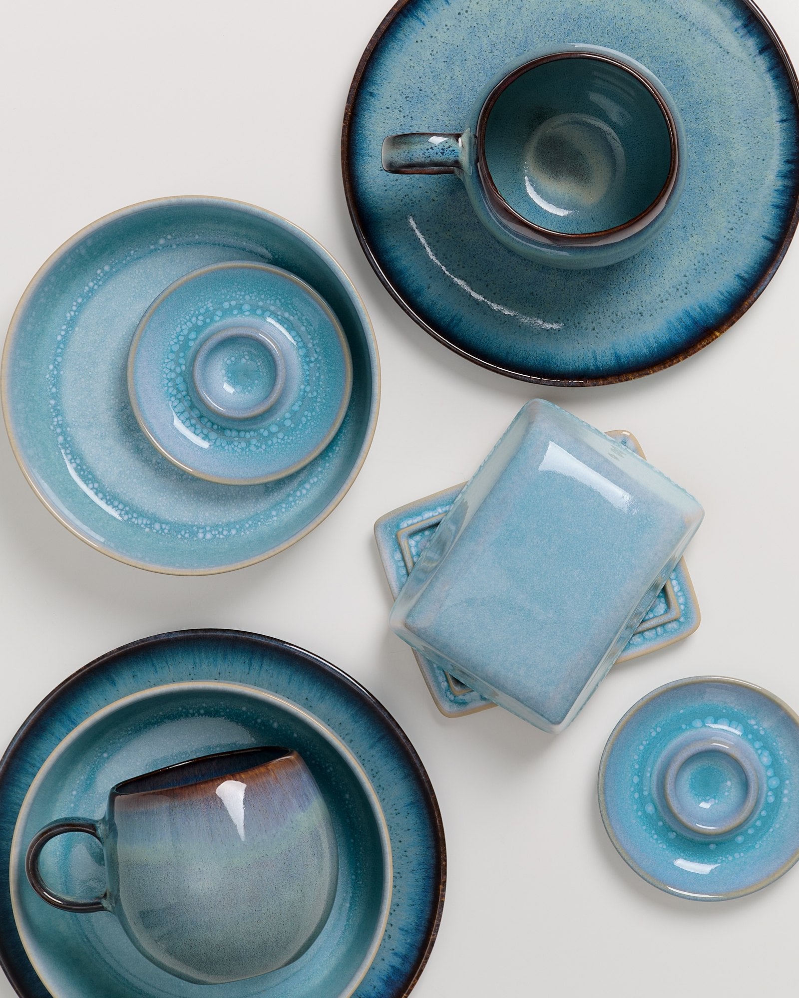 Verschiedenes blaues Keramikgeschirr, darunter Tassen, Teller und eine rechteckige Schale, auf weißem Hintergrund.