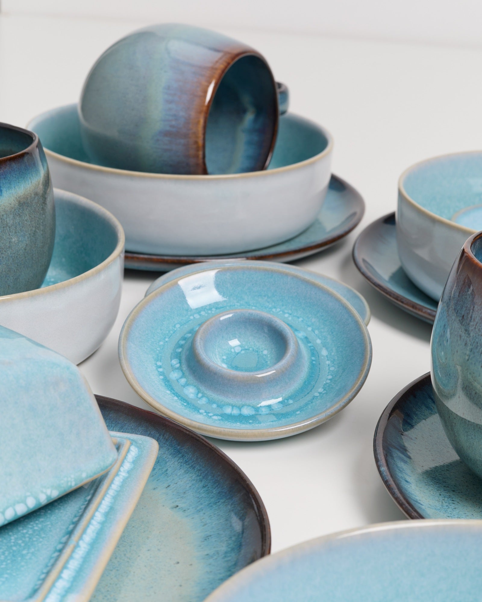 Keramikgeschirr in Blau- und Brauntönen auf einem weißen Untergrund, darunter Tassen, Teller und Schalen.