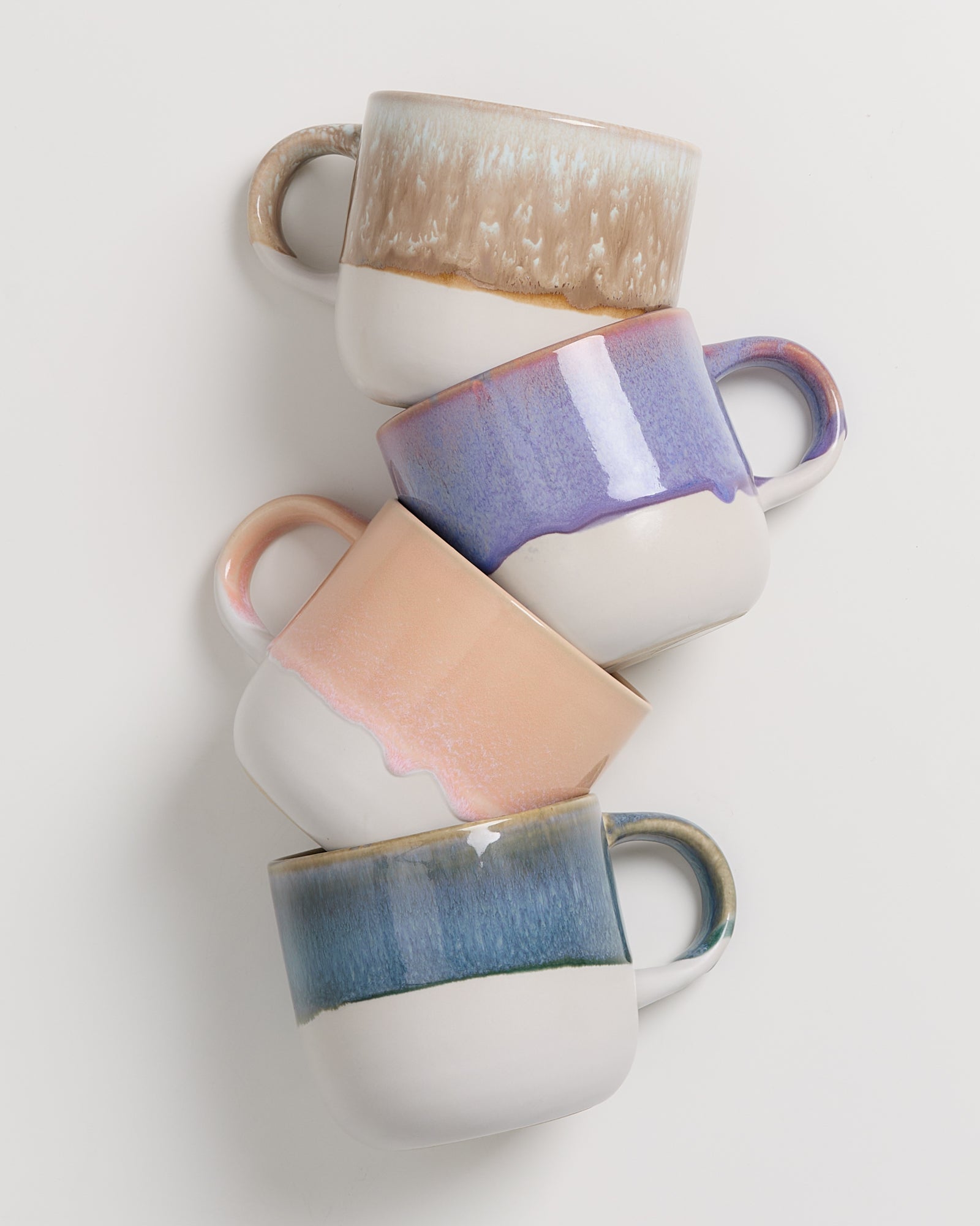 Vier gestapelte Keramiktassen in verschiedenen Farben auf weißem Hintergrund.