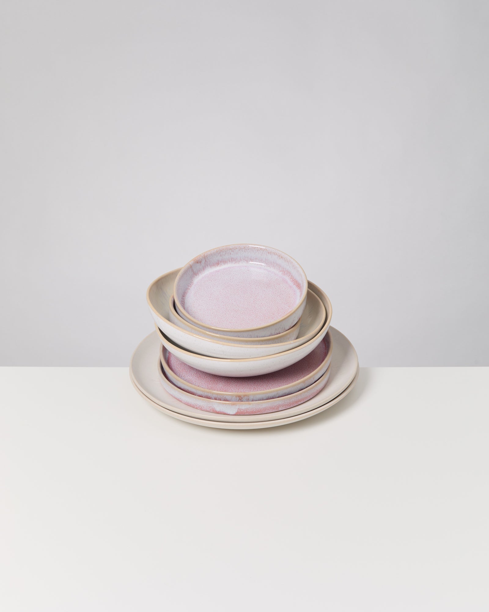 Ein Stapel Keramikteller und -schalen mit rosa Glasur steht auf einem weißen Tisch.