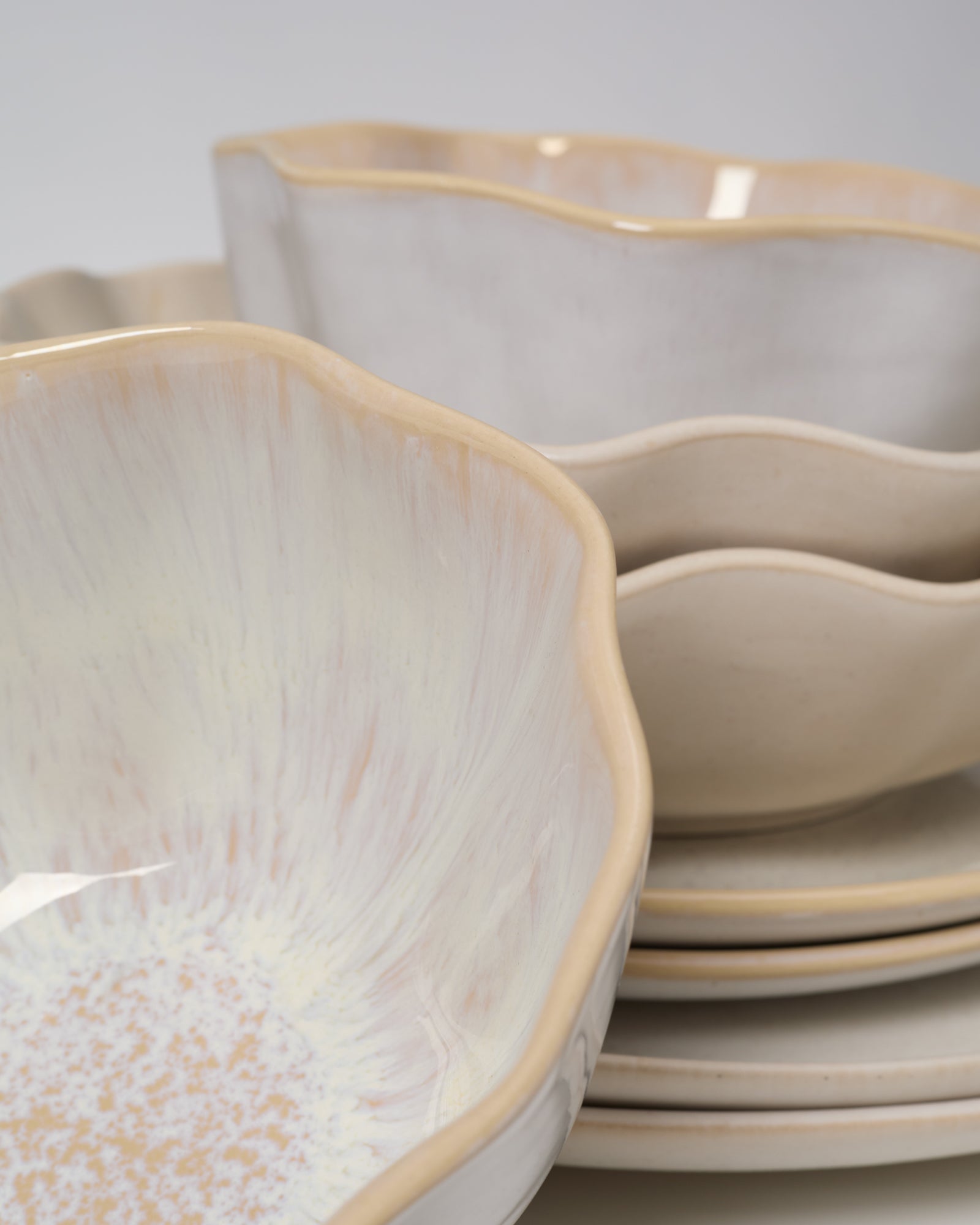 Keramikteller und -schalen mit welligem Rand und cremefarbener Glasur sind gestapelt.