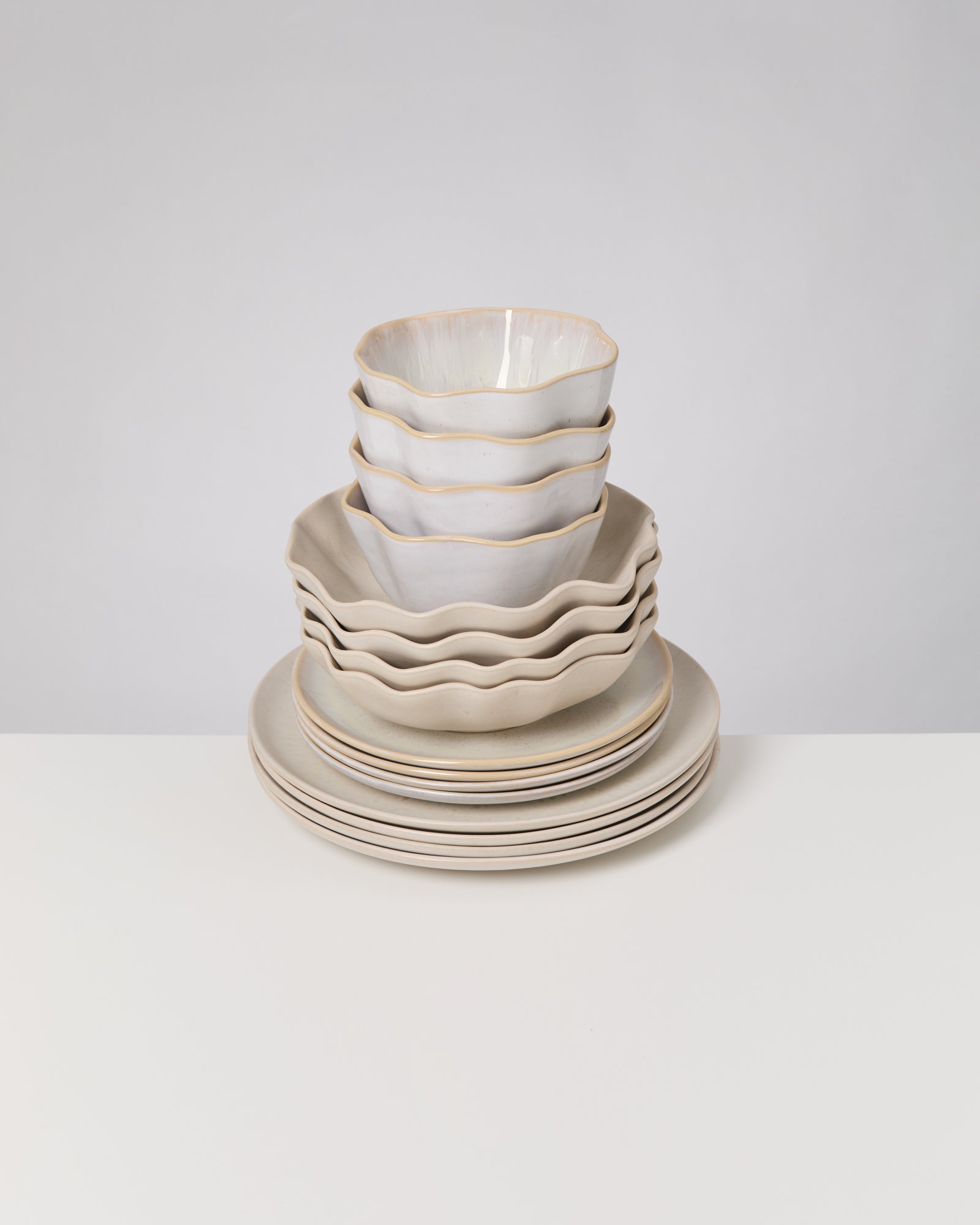 Gestapelte weiße Keramikschüsseln und Teller mit gewelltem Rand auf einem weißen Tisch.