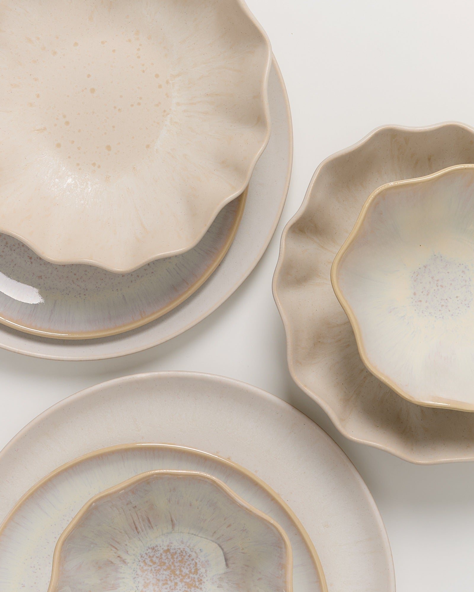 Beige Keramikgeschirr mit unregelmäßiger, gewellter Form auf weißem Hintergrund, teilweise übereinander gestapelt.