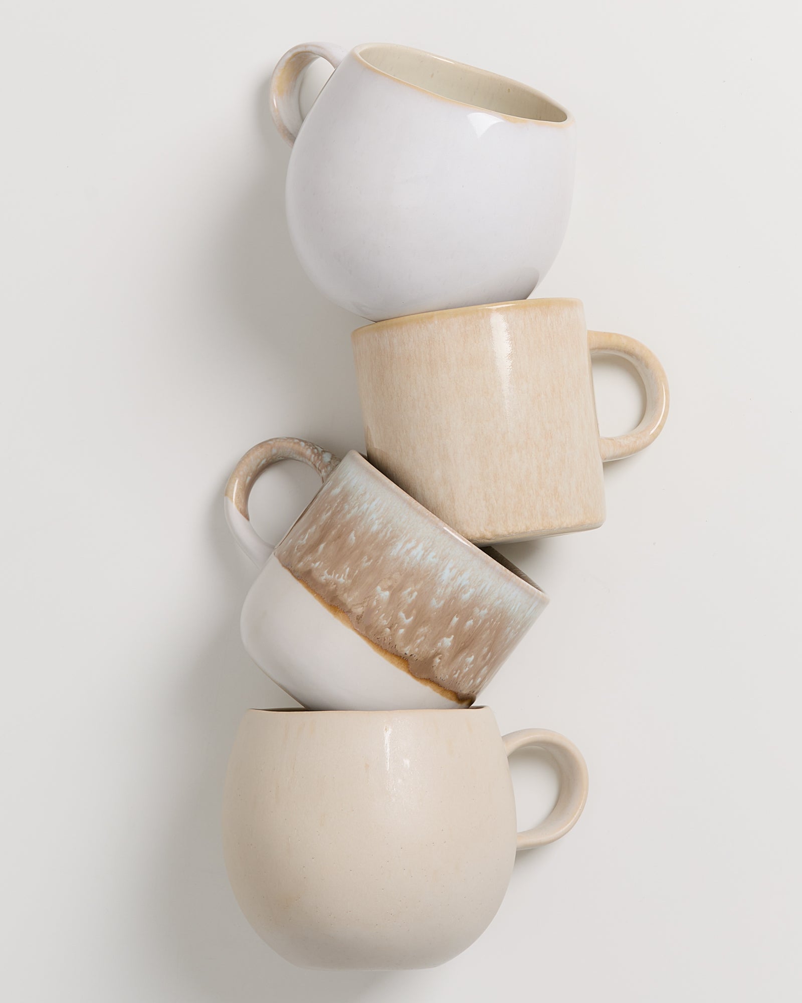 Vier gestapelte Tassen in verschiedenen Naturtönen auf weißem Hintergrund.
