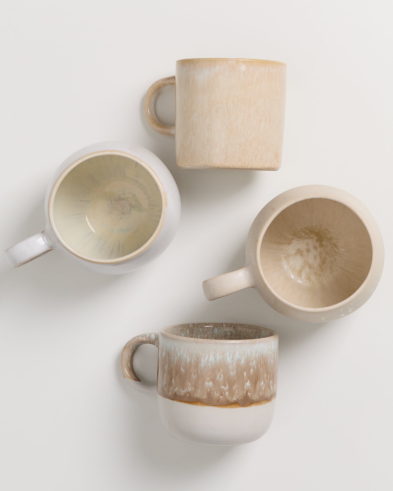 Vier Keramiktassen in natürlichen Farbtönen auf einer weißen Oberfläche angeordnet.