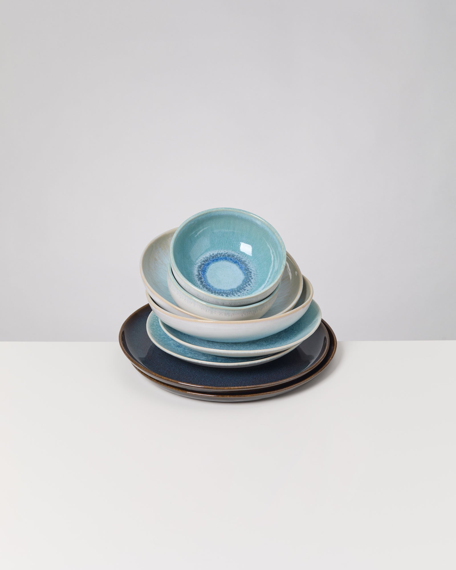 Ein Stapel blauer und weißer Keramikschüsseln und -teller auf weißem Tisch vor grauem Hintergrund.