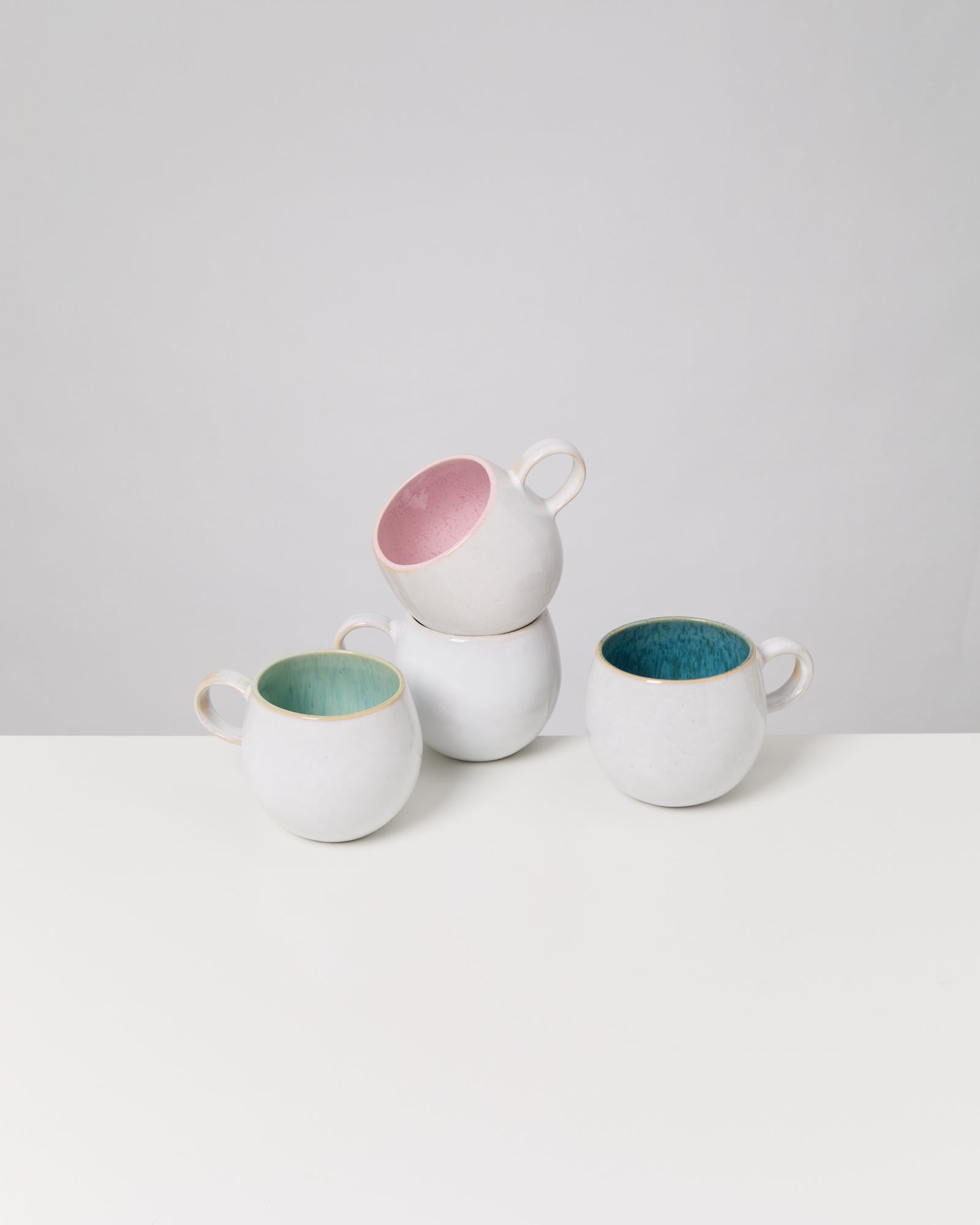 Vier stapelbare, weiße Tassen mit buntem Innenraum auf einem Tisch.