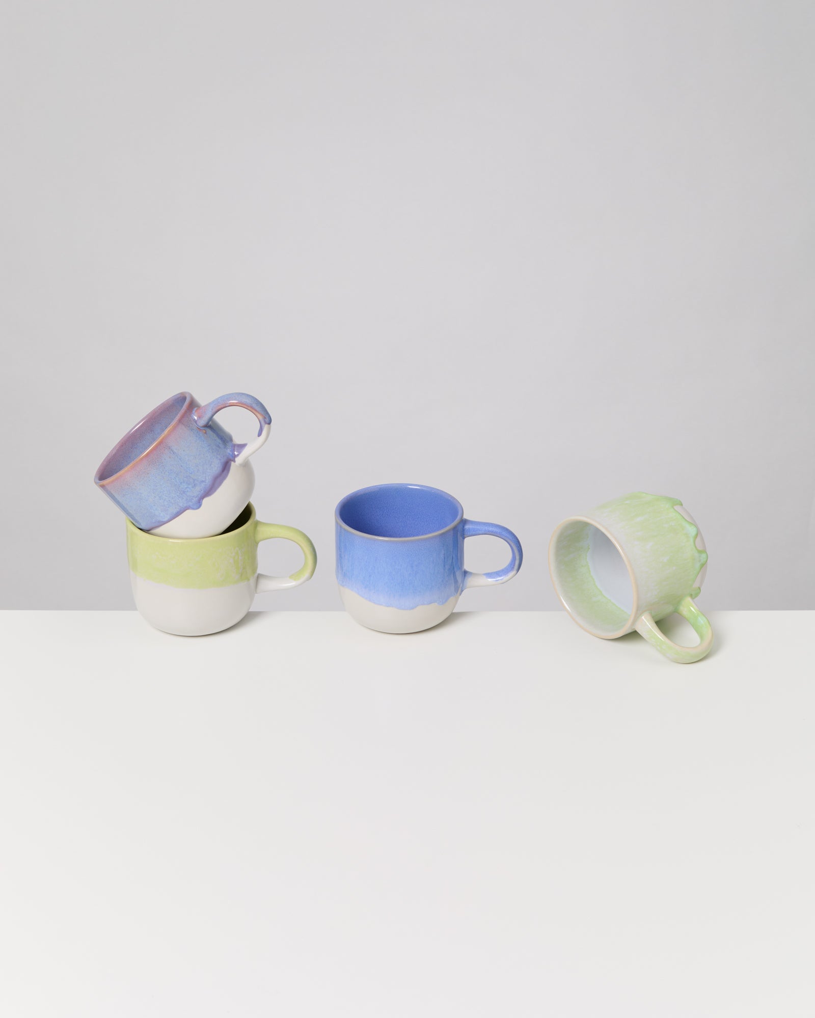 Vier bunte Keramiktassen auf einem weißen Tisch, eine Tasse liegt auf der Seite.