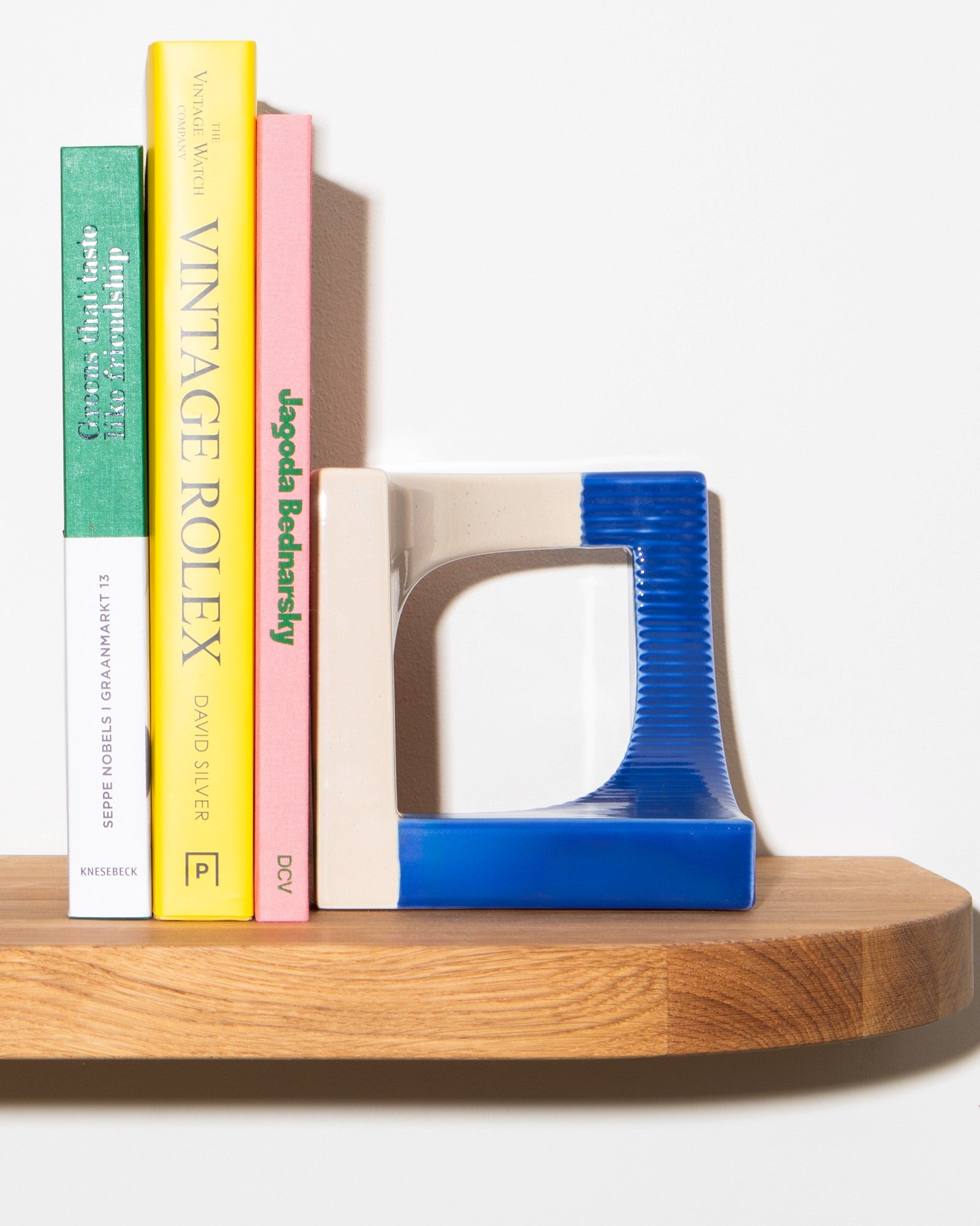 Bücher stehen auf einem Holzregal neben einem blauen Buchstützenobjekt.