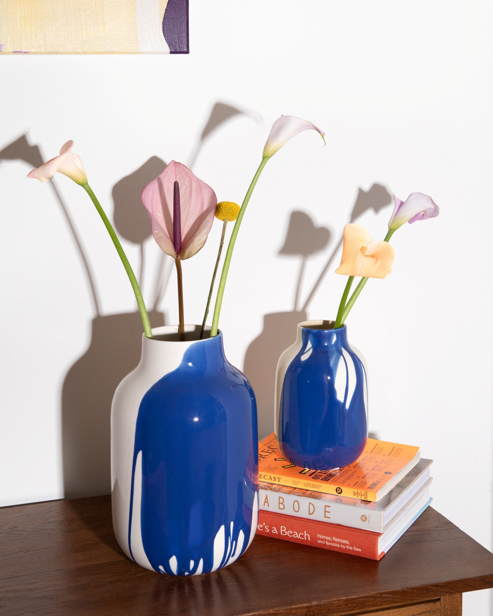 Zwei blaue Vasen mit Blumen stehen auf einem Holztisch, eine auf mehreren gestapelten Büchern.