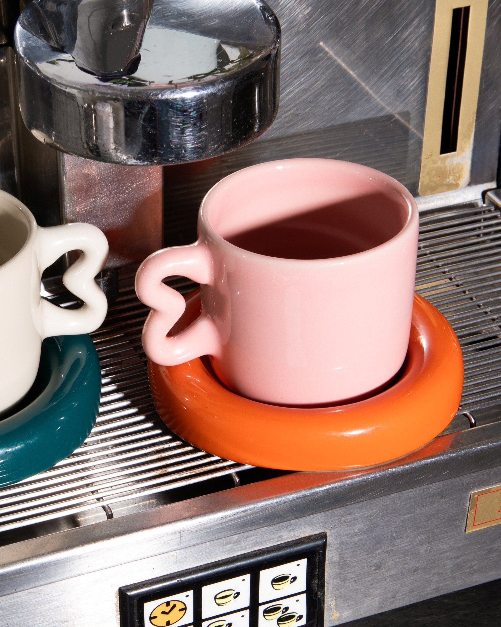 Zwei bunte Tassen mit ungewöhnlichen Henkeln stehen auf einer Espressomaschine.